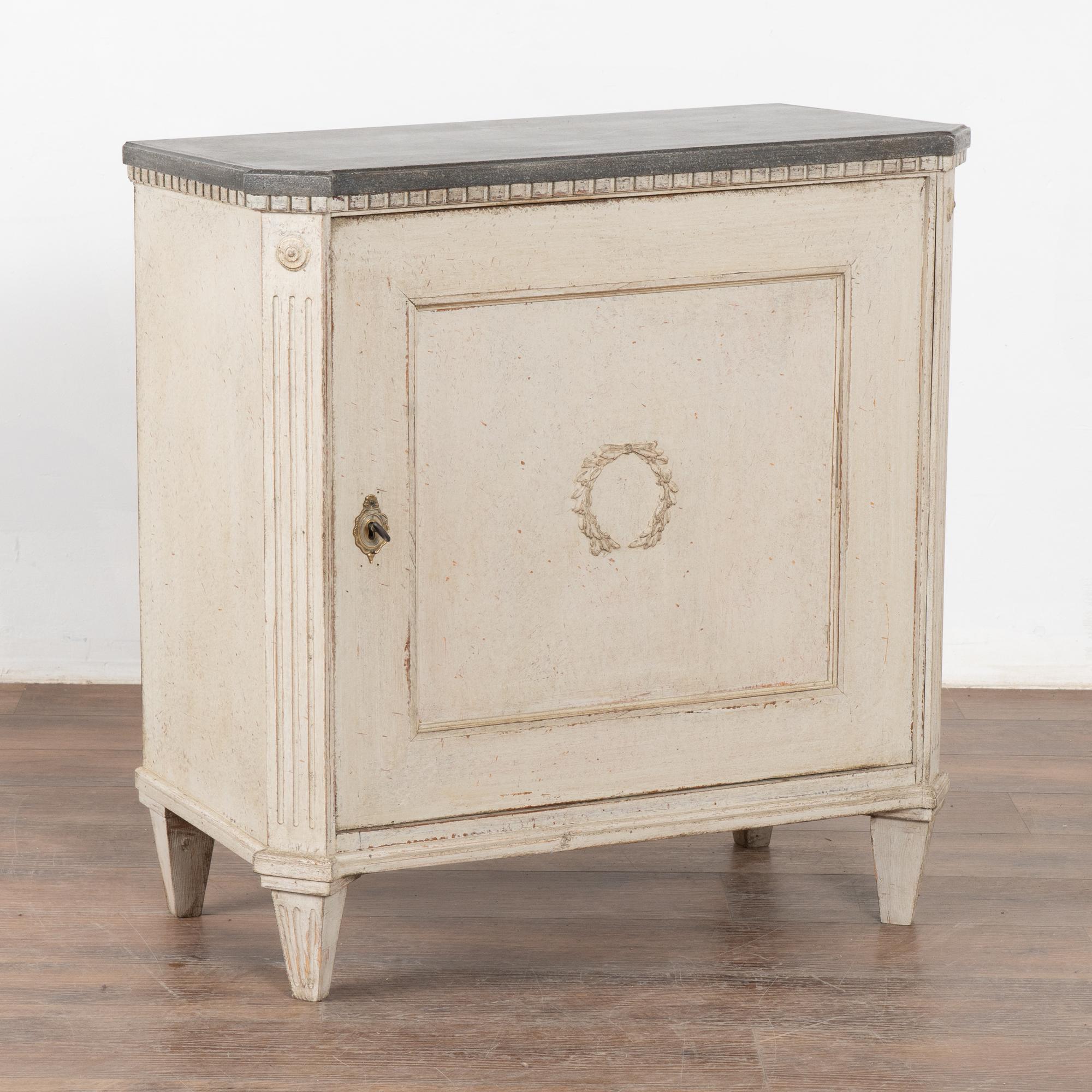 Petite armoire aux côtés cannelés et à la moulure en denticule, reposant sur des pieds fuselés et cannelés.
La serrure fonctionne avec une clé incluse. Une seule étagère intérieure est également incluse.
La nouvelle finition peinte en blanc antique