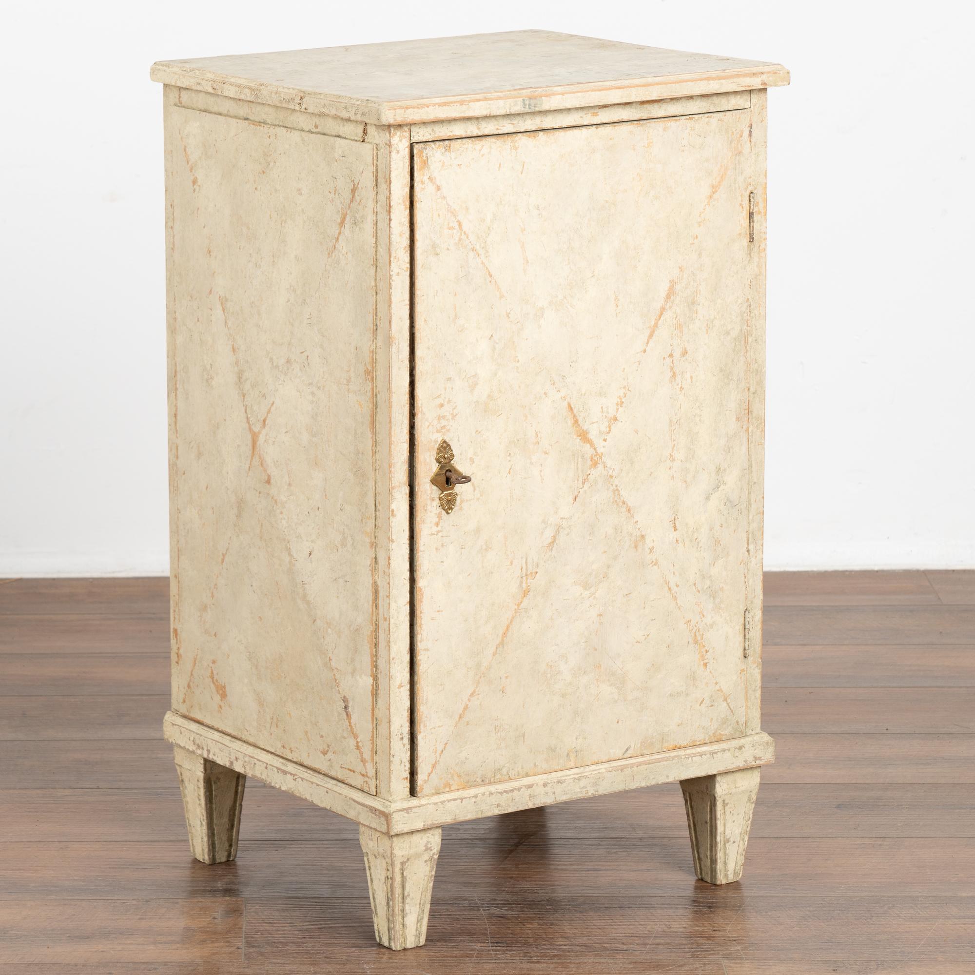 Small Swedish country antique white painted nightstand or side table standing on fluted tapered feet. May have served as a music cabinet to store sheet music.
Slightly raised diamond motif on front panel door and sides. Gentle distressing to the