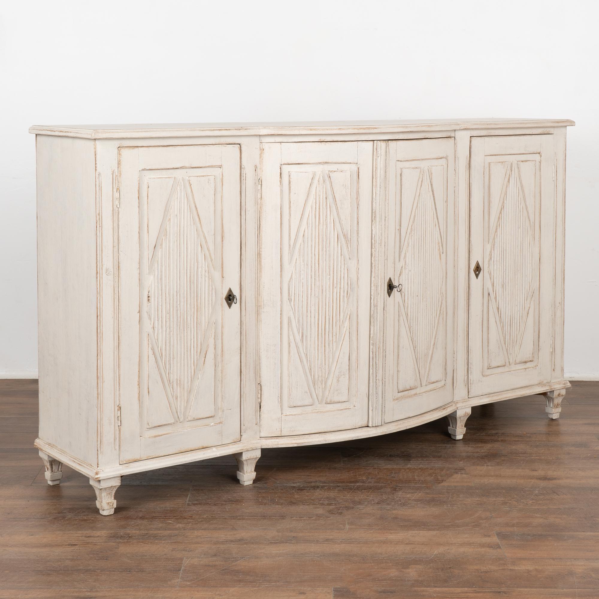 Swedish 5.5' long Gustavian pine sideboard buffet server with traditional carved fluted diamond panel motif on each of the four doors.
Tapered fluted feet. Central 2 cabinet doors bow slightly outward. Door latches function, two keys included. One