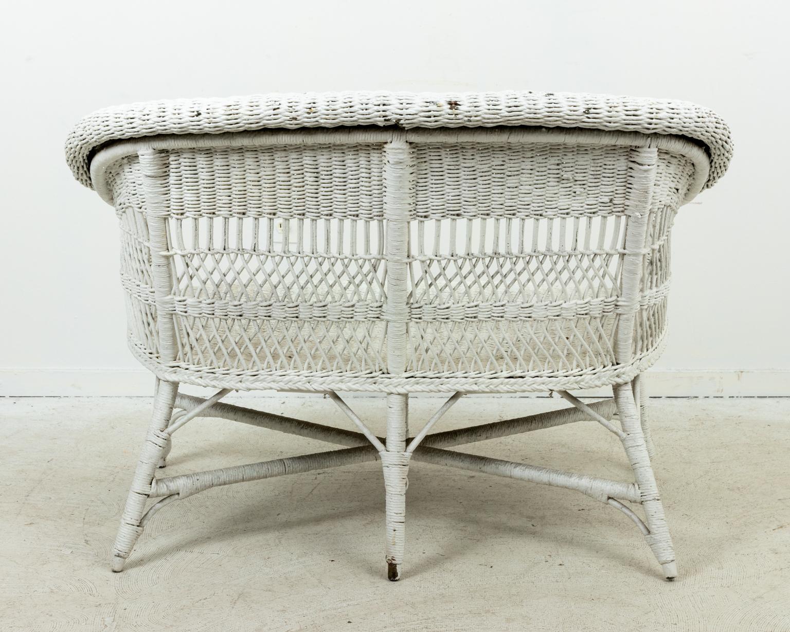Vintage white painted wicker settee with woven lattice work detail, circa 1930s. Made in the United States. Please note of wear consistent with age including minor paint loss. There are a few area on the seat and back that show wear to the