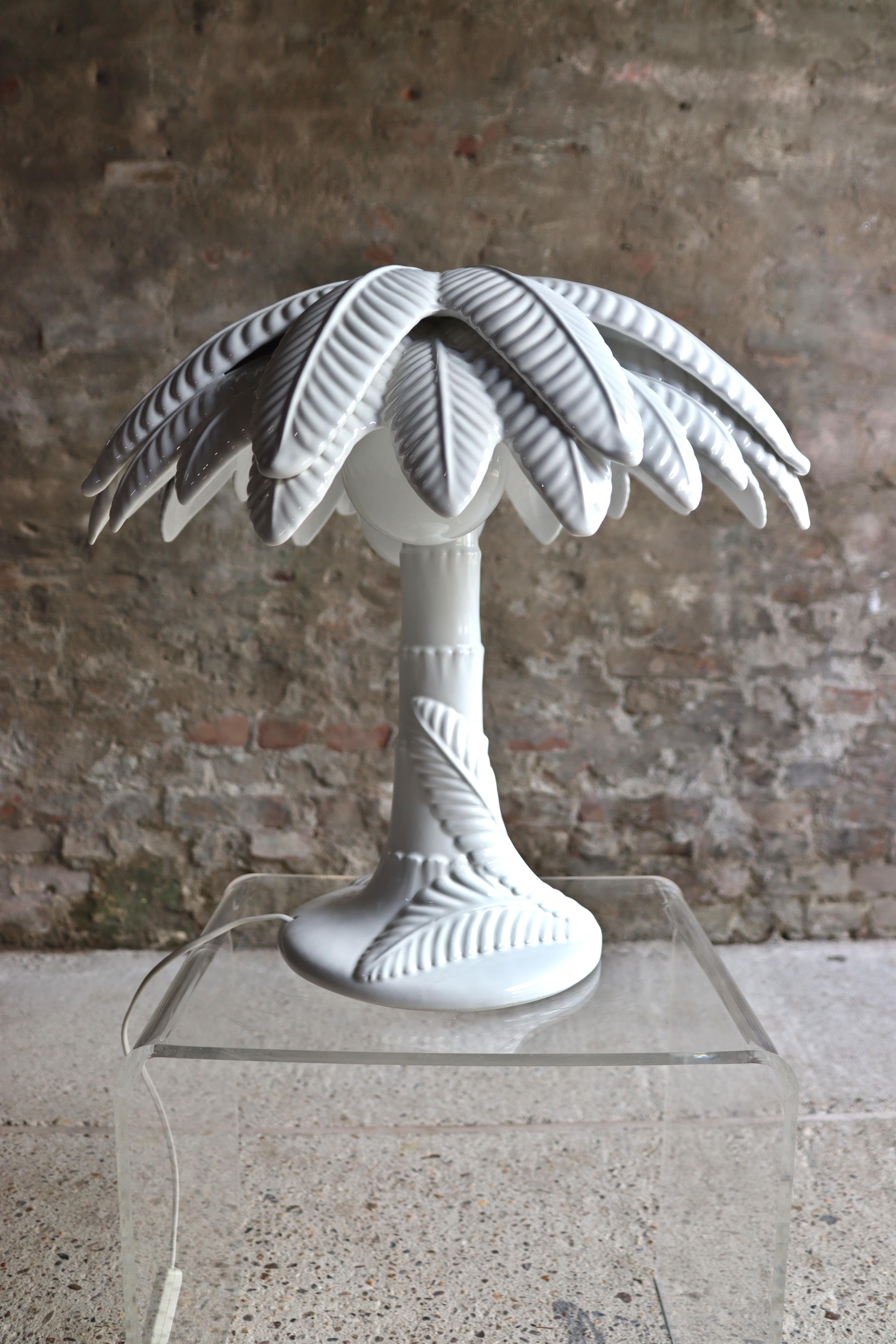 Cette lampe en forme de palmier blanc très cool a une base en céramique et des feuilles en métal. La lampe a deux sources lumineuses et porte en dessous le cachet 
