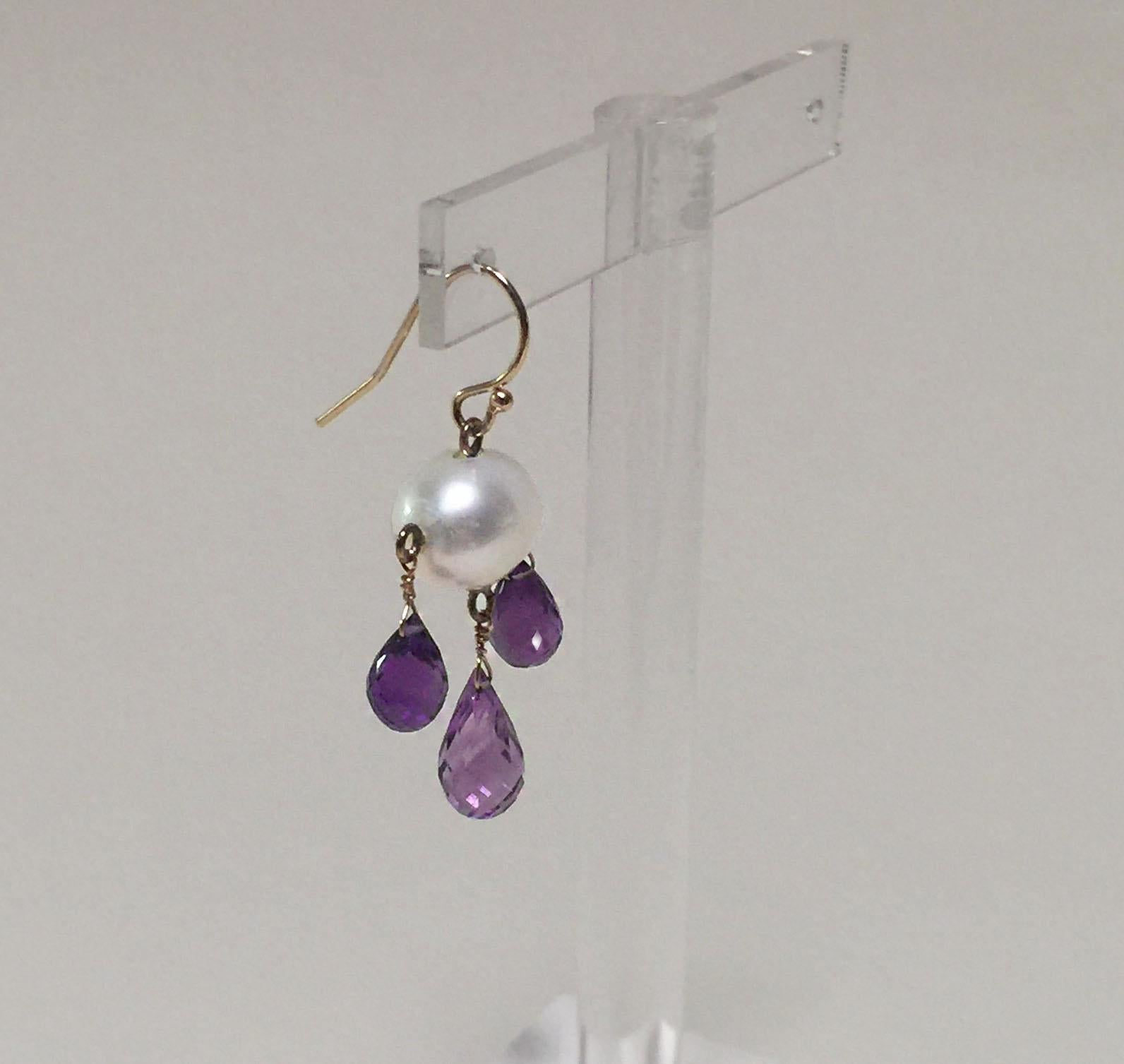 These white oval cultured pearl and amethyst drop earrings with 14 k yellow gold wiring and hook have a graceful look to them. At 1.8 inches long the earring classically frame the face. The 1 mm x 1.3 mm white pearl glows in contrast to the purple