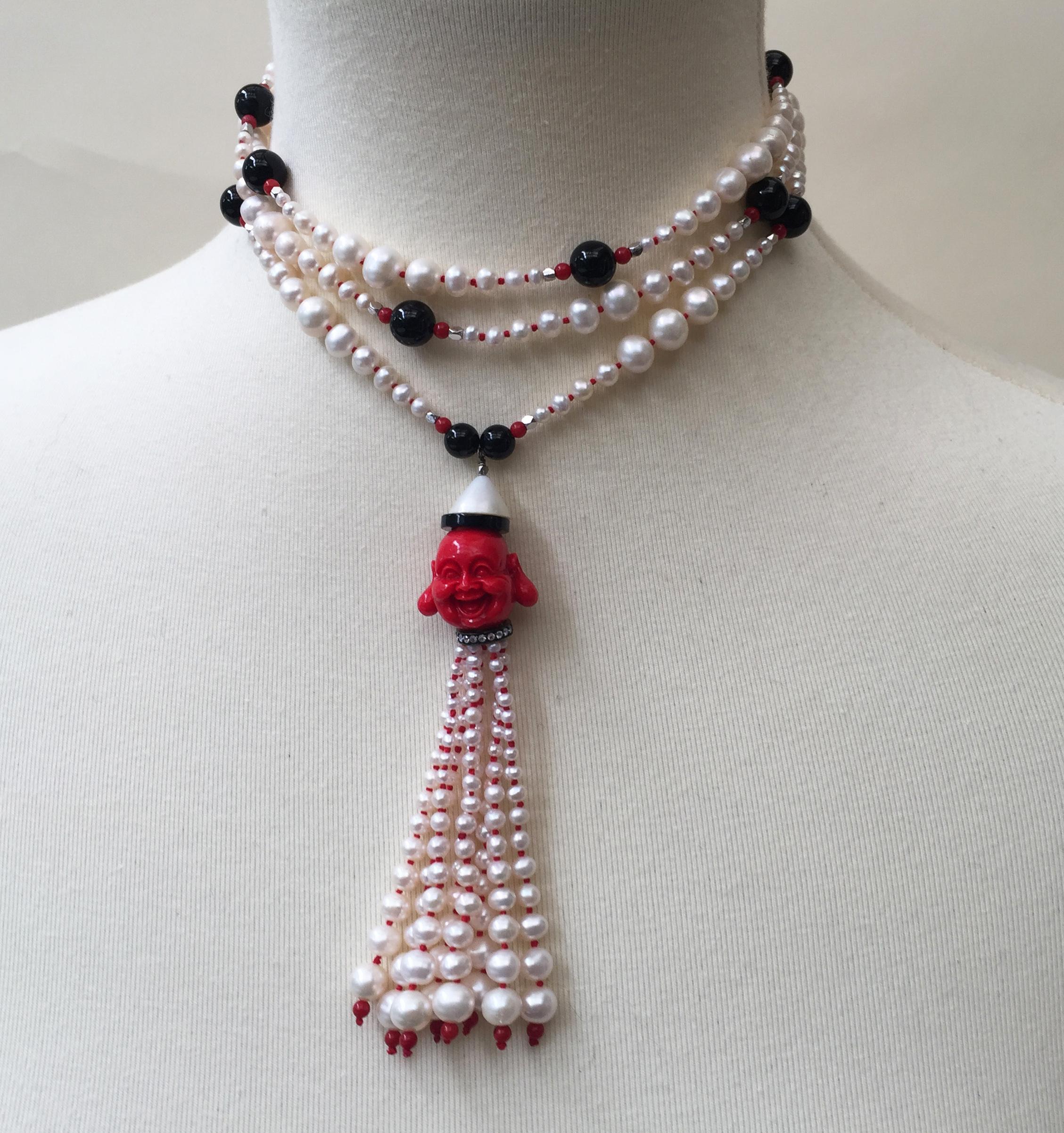 This sautoir necklace is composed of a long strand of graduated white pearls (2 mm-6 mm), coral, onyx, and sterling silver (rhodium plated) beads. At the center of the piece is a laughing coral Buddha bead, topped with onyx and a half white pearl.