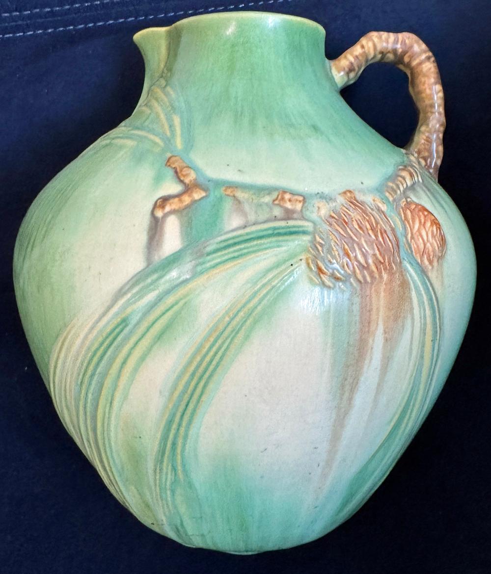 Inusuale per dimensioni e forma, questo grande vaso Art Déco a forma di brocca presenta rami di pino con stravaganti spruzzi di aghi di pino e pigne, il tutto espresso in ricchi smalti verde smeraldo e nero-marrone. Questa linea di ceramiche è stata