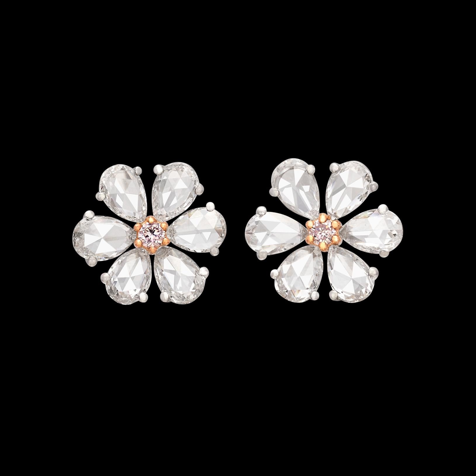 A floral stud with a pop of colored diamond in the center! These 18 karat white gold stunners feature six expertly cut pear shaped diamond petals on each ear, with a natural pink round brilliant cut diamond making up the center of the flower design.