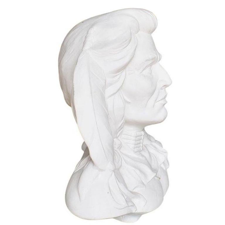 Cast in pure white plaster, this bust sculpture depicts the face of a Native American warrior. His long hair is pulled to the side and tied with trompe l'oeil leather strips. He wears an ornate necklace and has a feather in his hair. This piece is
