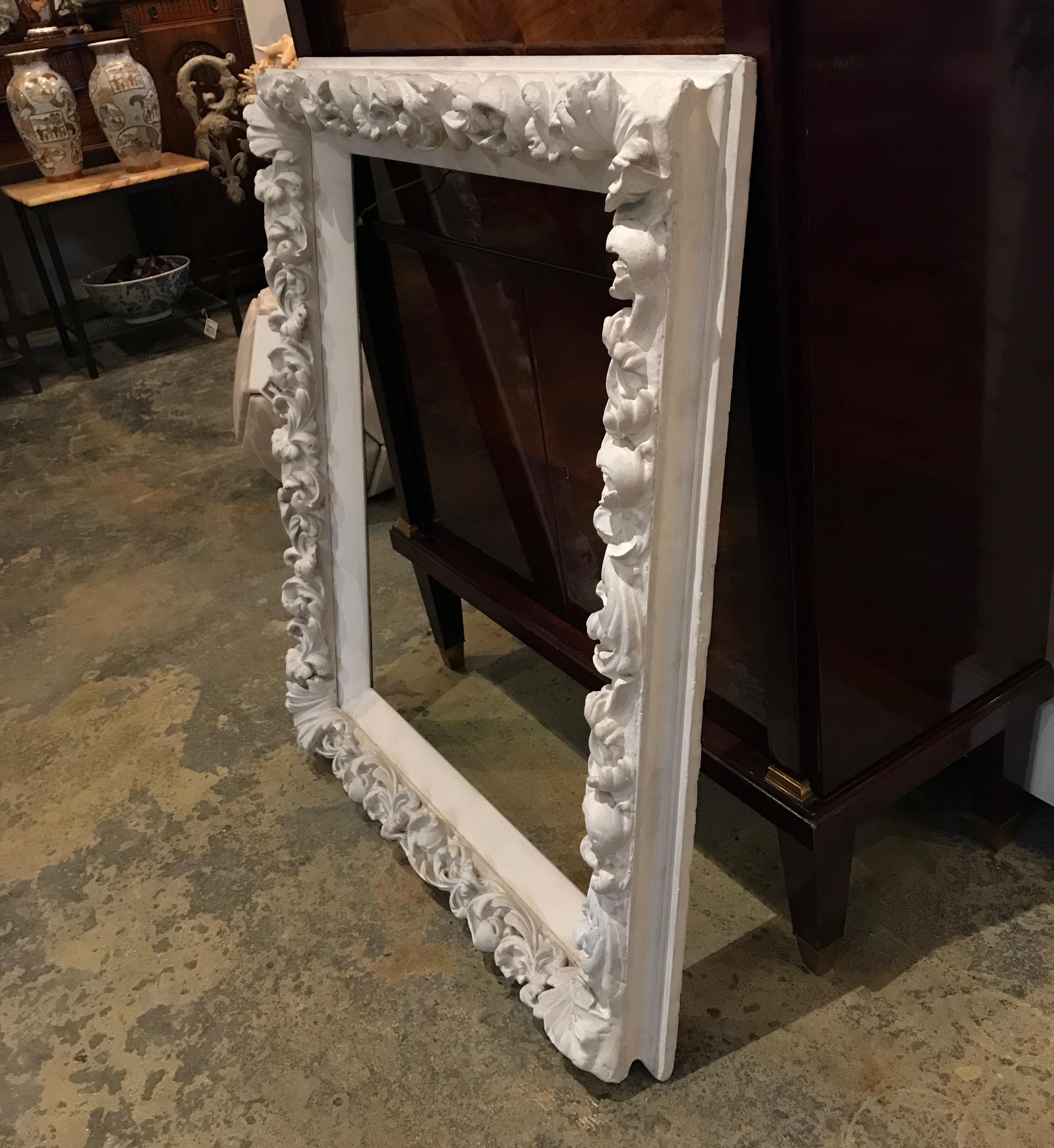 This thick, large wooden frame is hand carved and painted in a white plaster like paint to match the protruding sweeping and flowing plaster-made floral and leafy shapes.