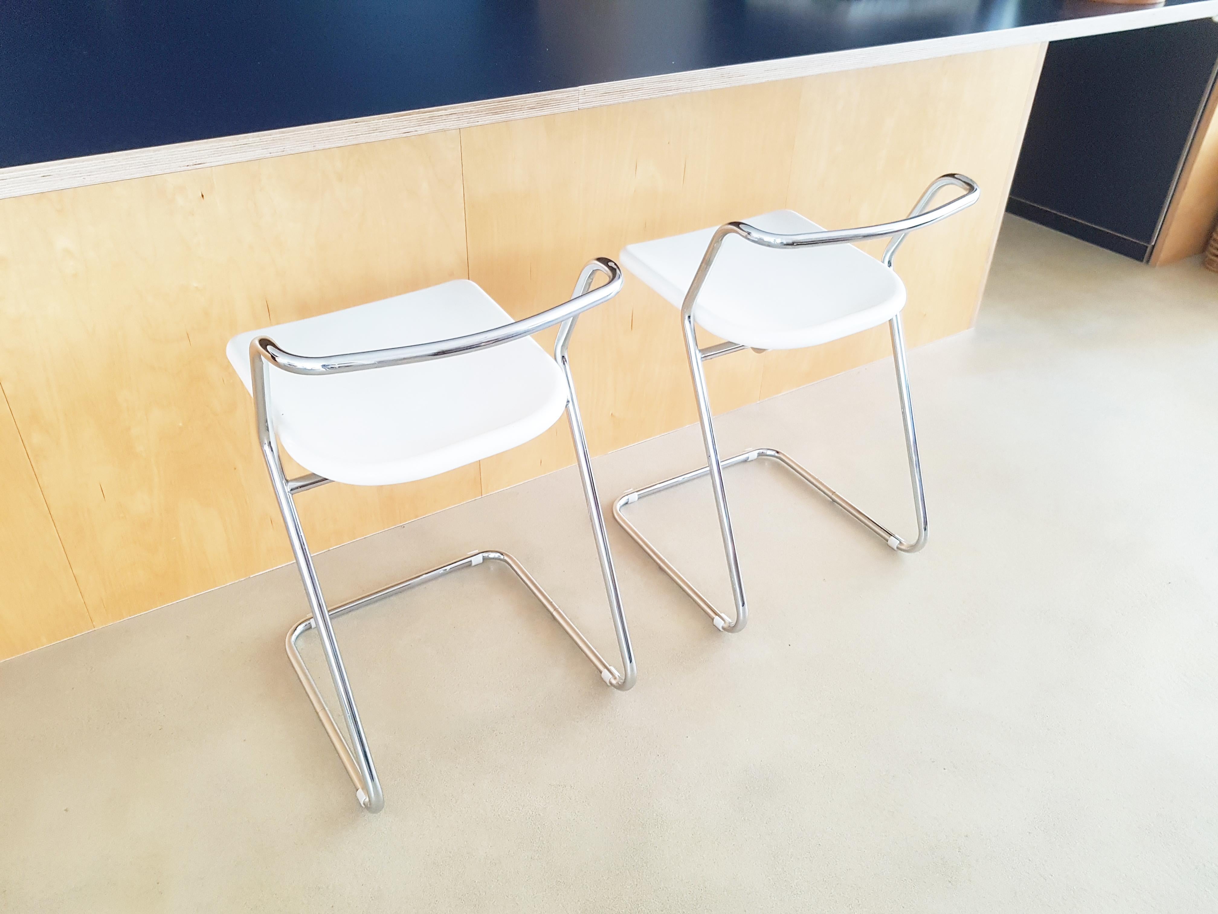 Coppia di sgabelli con supporto tubolare cromato e seduta pieghevole in plastica (forse resina di vetro) verniciata di bianco. Questi sedili spessi sono ergonomici e progettati per essere ripiegati. La struttura tubolare conferisce un buon comfort