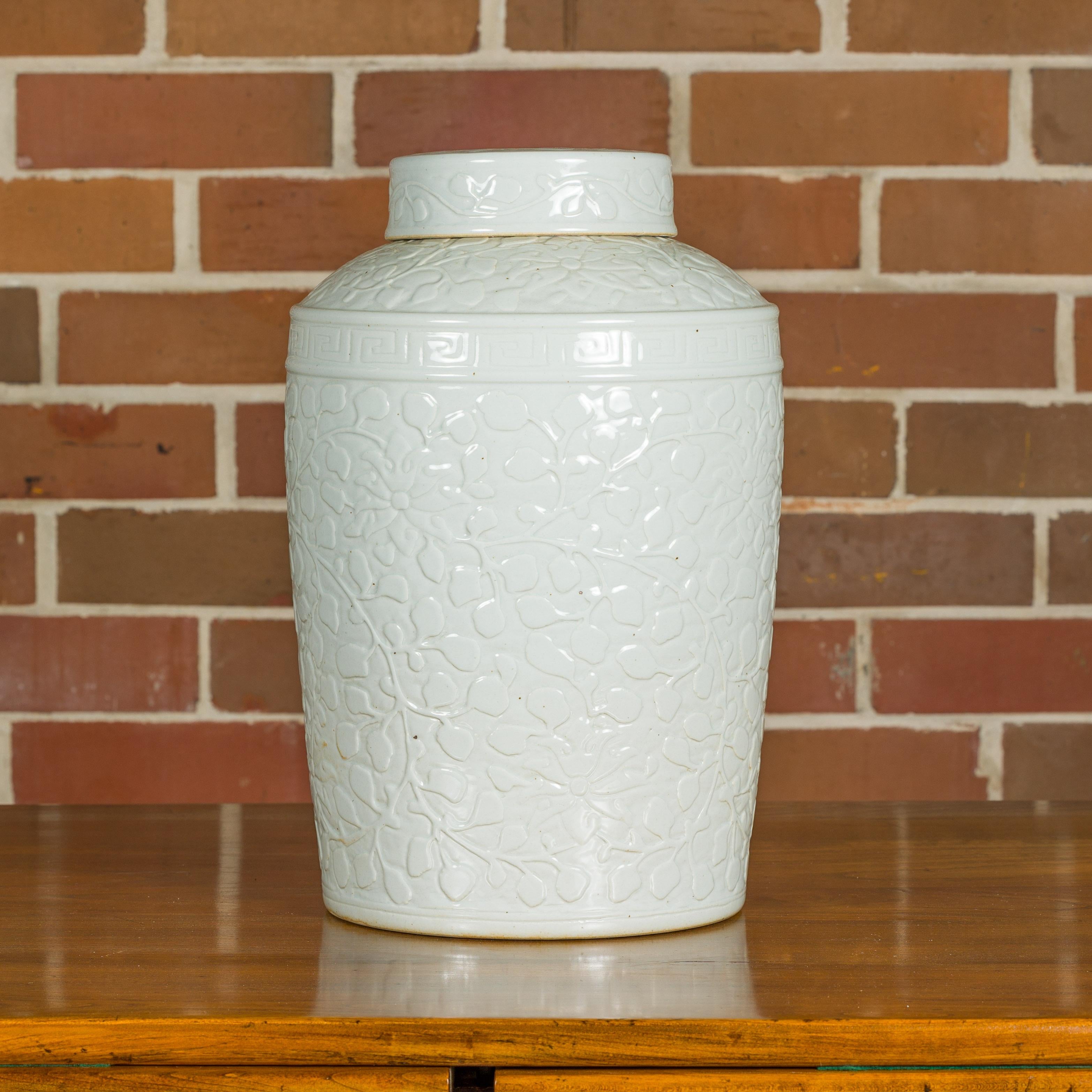 A white porcelain Asian lidded jar with scrolling foliage motifs and slightly tapering lines. This exquisite white porcelain Asian lidded jar is a splendid example of timeless elegance and delicate artistry. The jar features beautifully scrolling