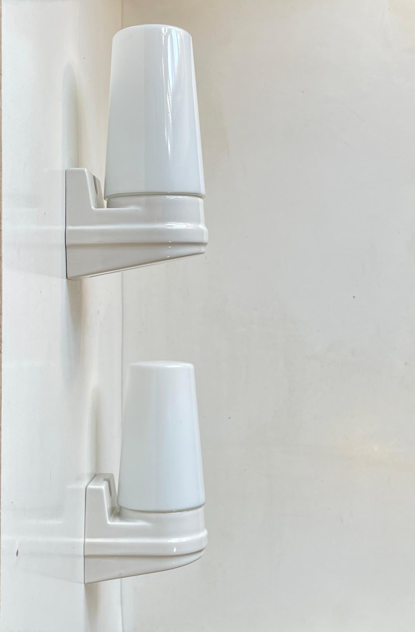 A pair of sconces suitable as bathroom or outdoor lighting. They were designed by Prince Sigvard Bernadotte for the swedish company Ifö during the 1960s. White glazed porcelain mounts with white opaline glass shading. 2 way mount - either shade