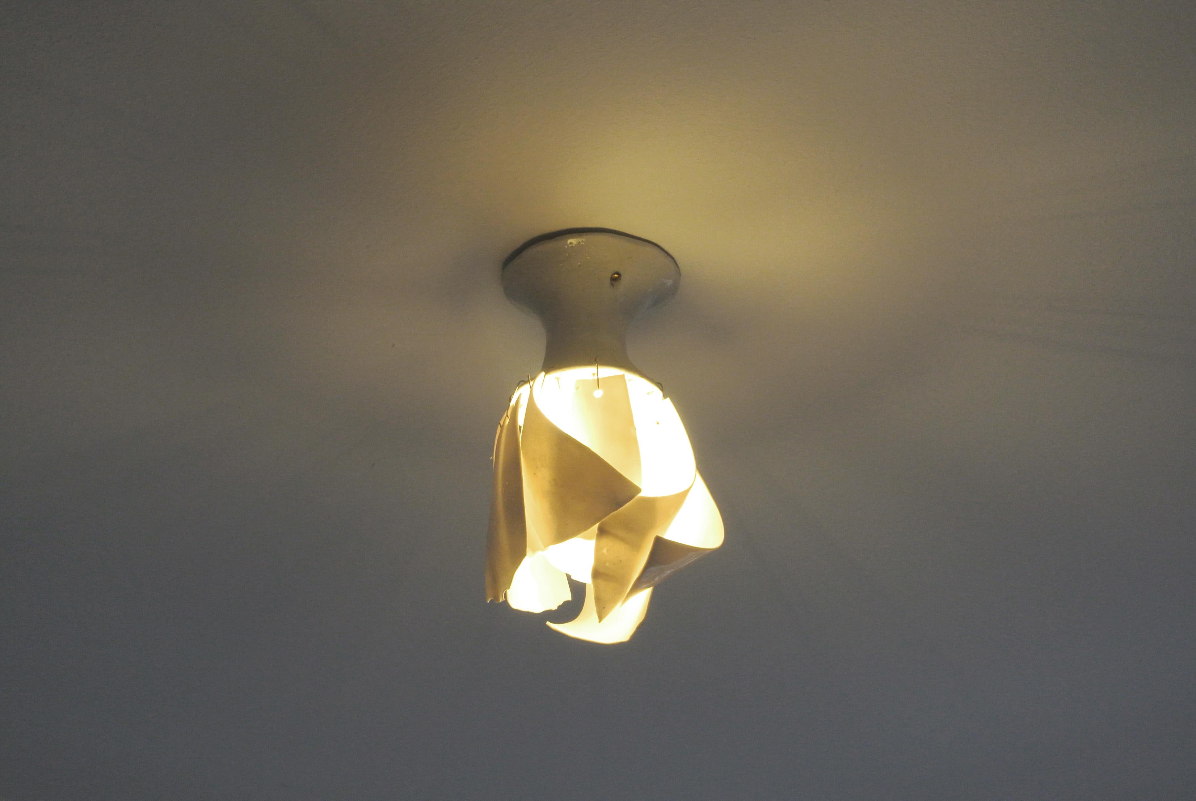Hand build porcelain lamp fixture with glossy white glaze. White porcelain petals hang from metal hooks attached to the fixture, these are not permanently fixed.
The petals surround the light bulb in a rounded, asymmetric shape.
This ceiling lamp