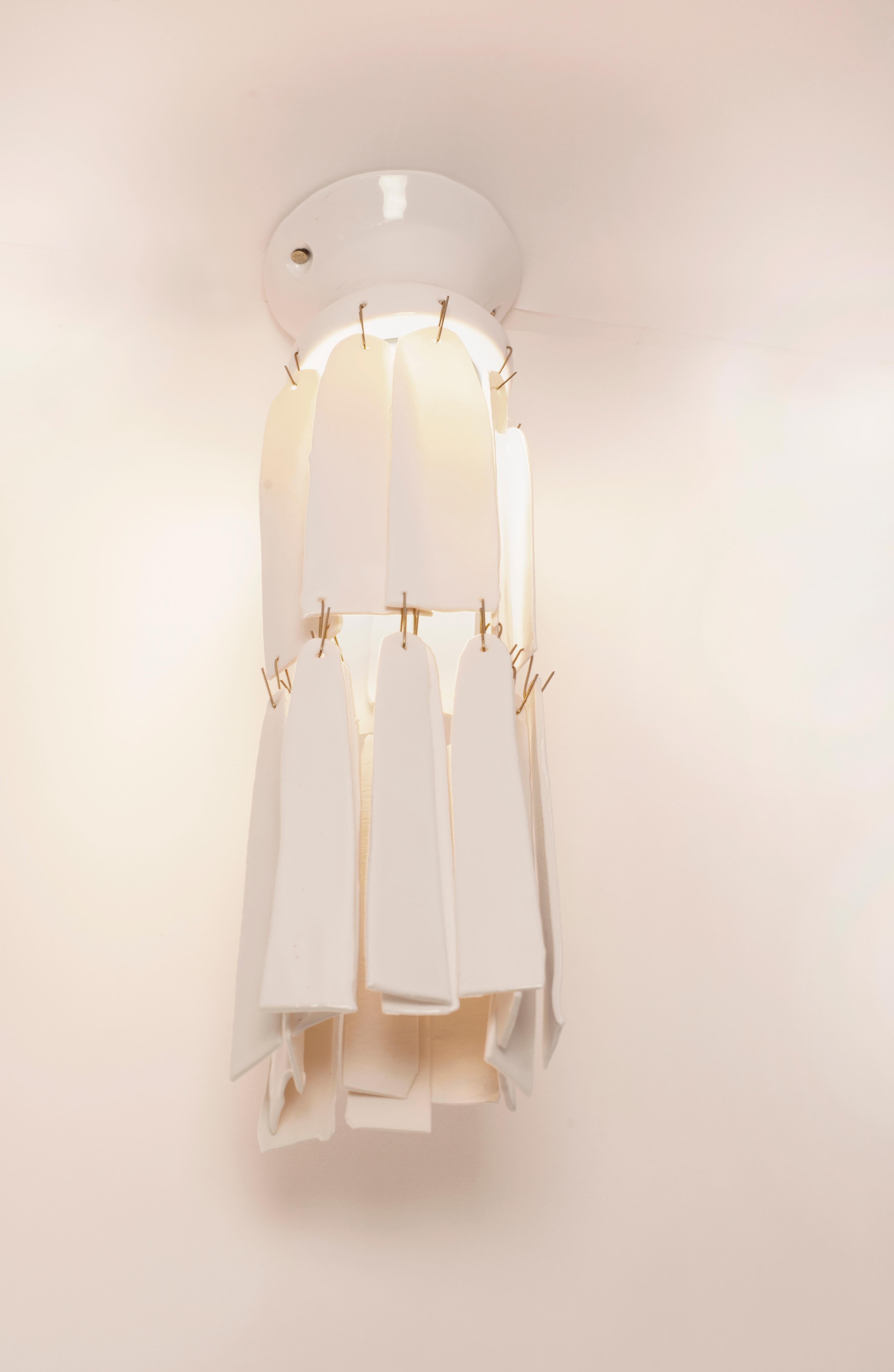 White lamp with hanging elements that reflect the light on the wall and ceiling. White Porcelain with White Glossy Glaze and Brass Hooks.