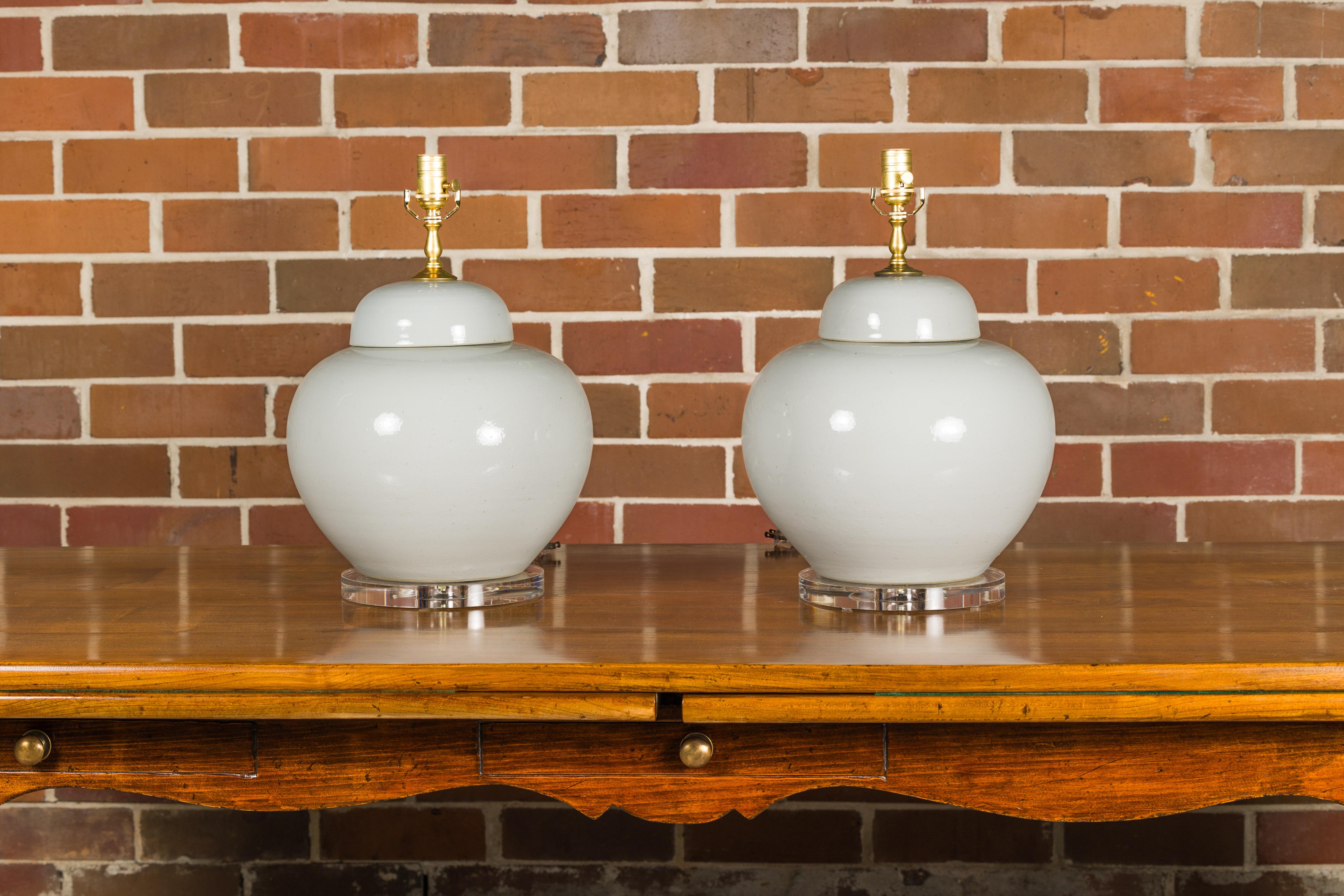A pair of white porcelain vases made into table lamps wired for the USA and mounted on lucite circular bases. Elevate your home decor with this exquisite pair of table lamps, masterfully transformed from white porcelain vases. Set upon lucite