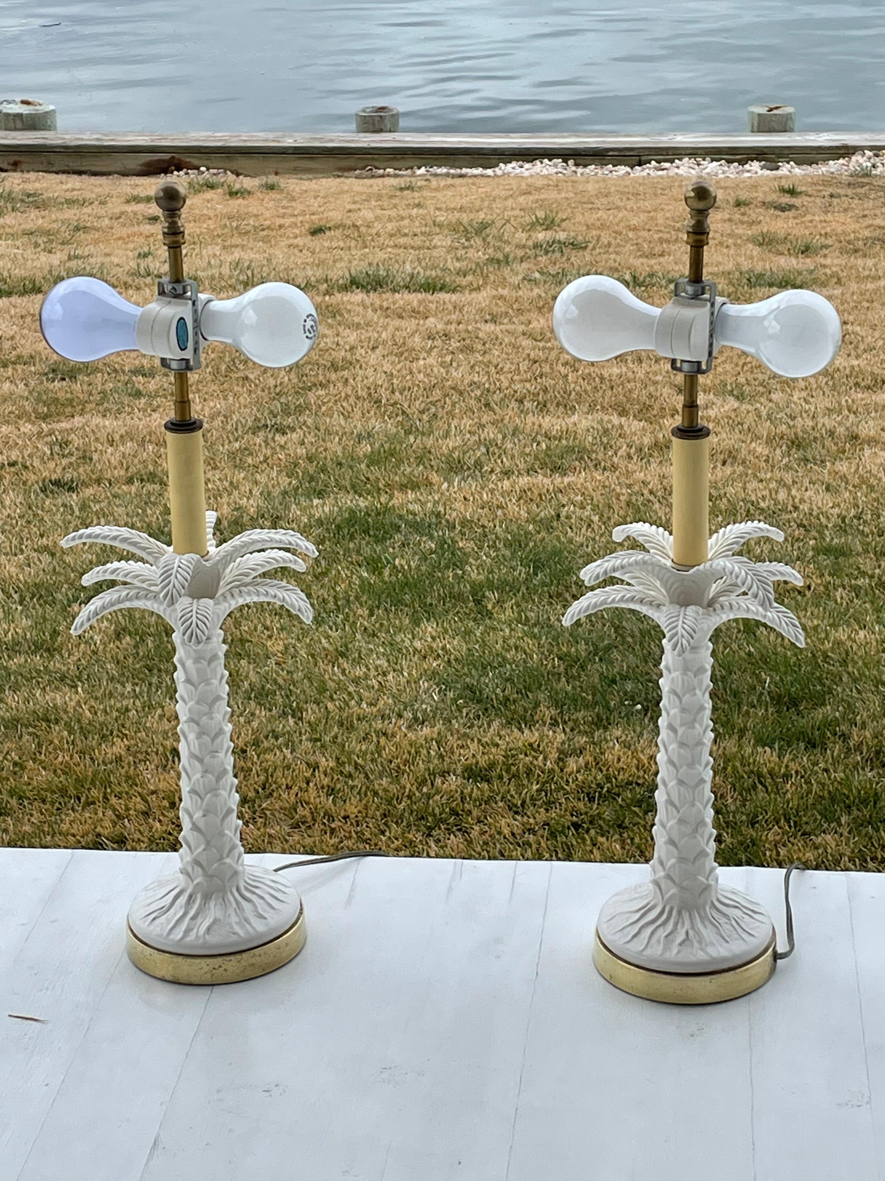 Pair of lovely white porcelain palm tree table lamps in the style of Hollywood Regency. There are two sets of detailed porcelain palm leaves and a bark pattern on the trunk and base . Two separate bulbs on each lamp that can be adjusted for