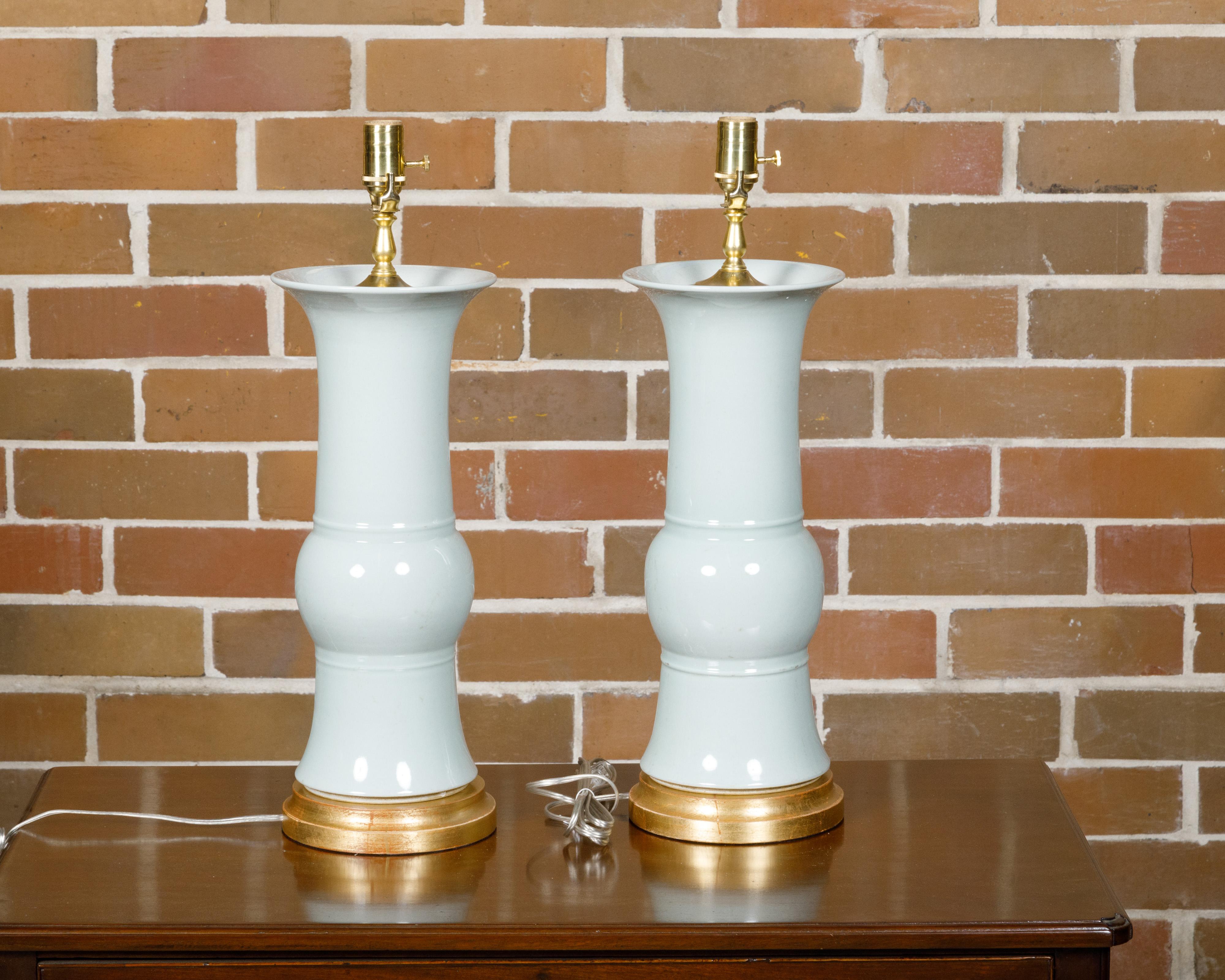 A pair of white porcelain table lamps on custom giltwood circular bases, professionally rewired for the USA. This elegant pair of white porcelain table lamps, set on custom giltwood circular bases, exudes a timeless charm and sophistication.