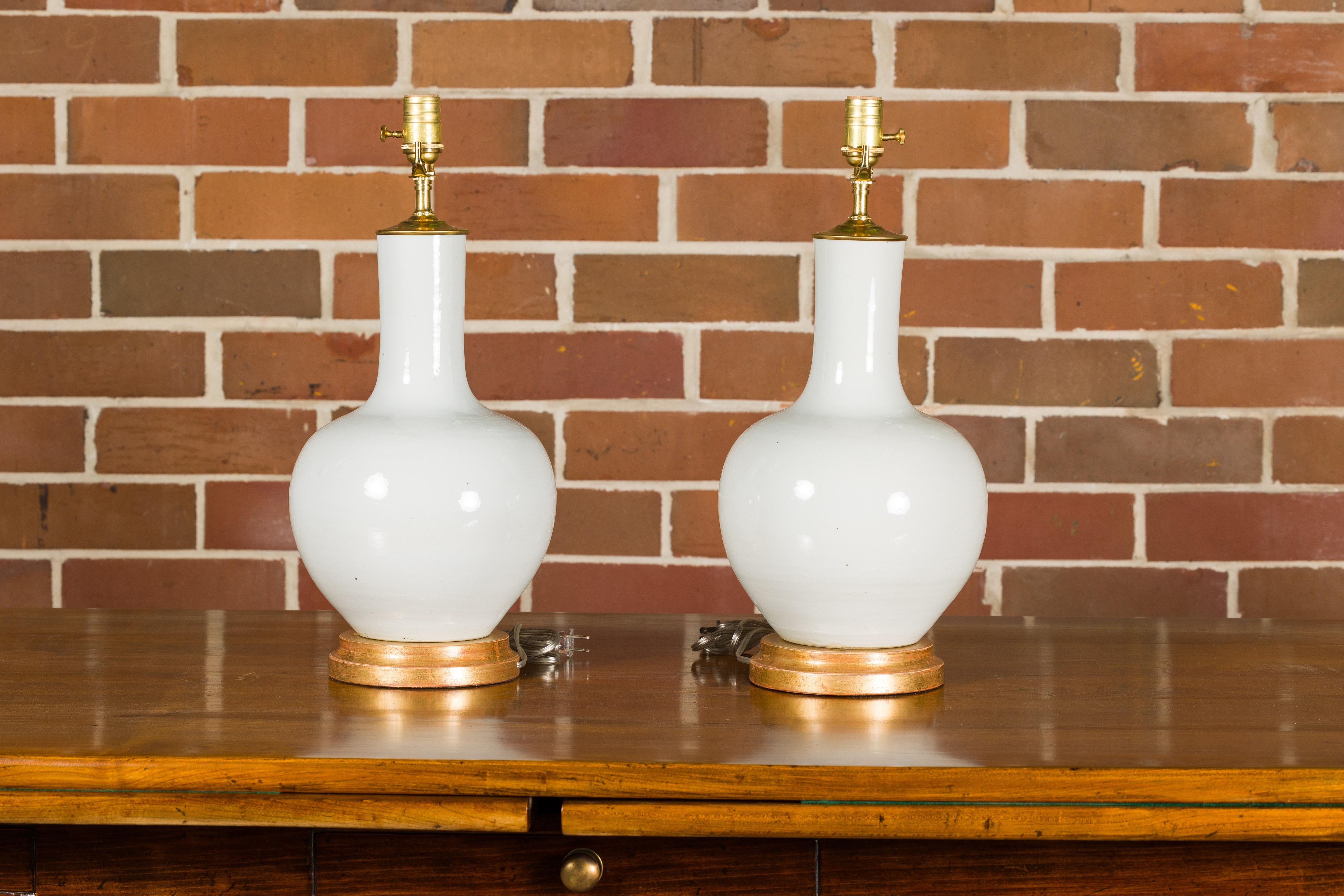 20ième siècle Paire de vases en porcelaine blanche transformés en lampes de table câblées sur bases en bois doré en vente