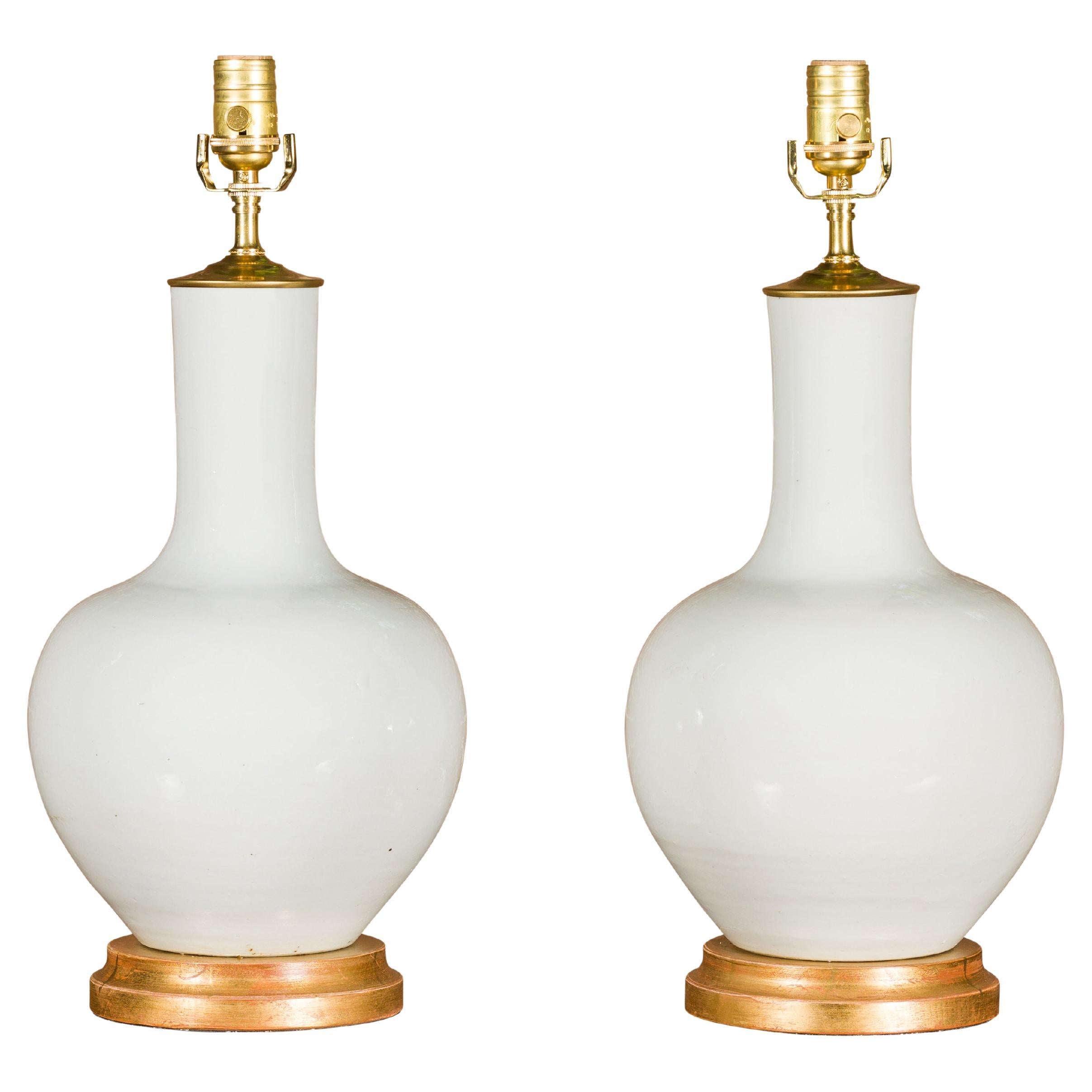 Paire de vases en porcelaine blanche transformés en lampes de table câblées sur bases en bois doré en vente
