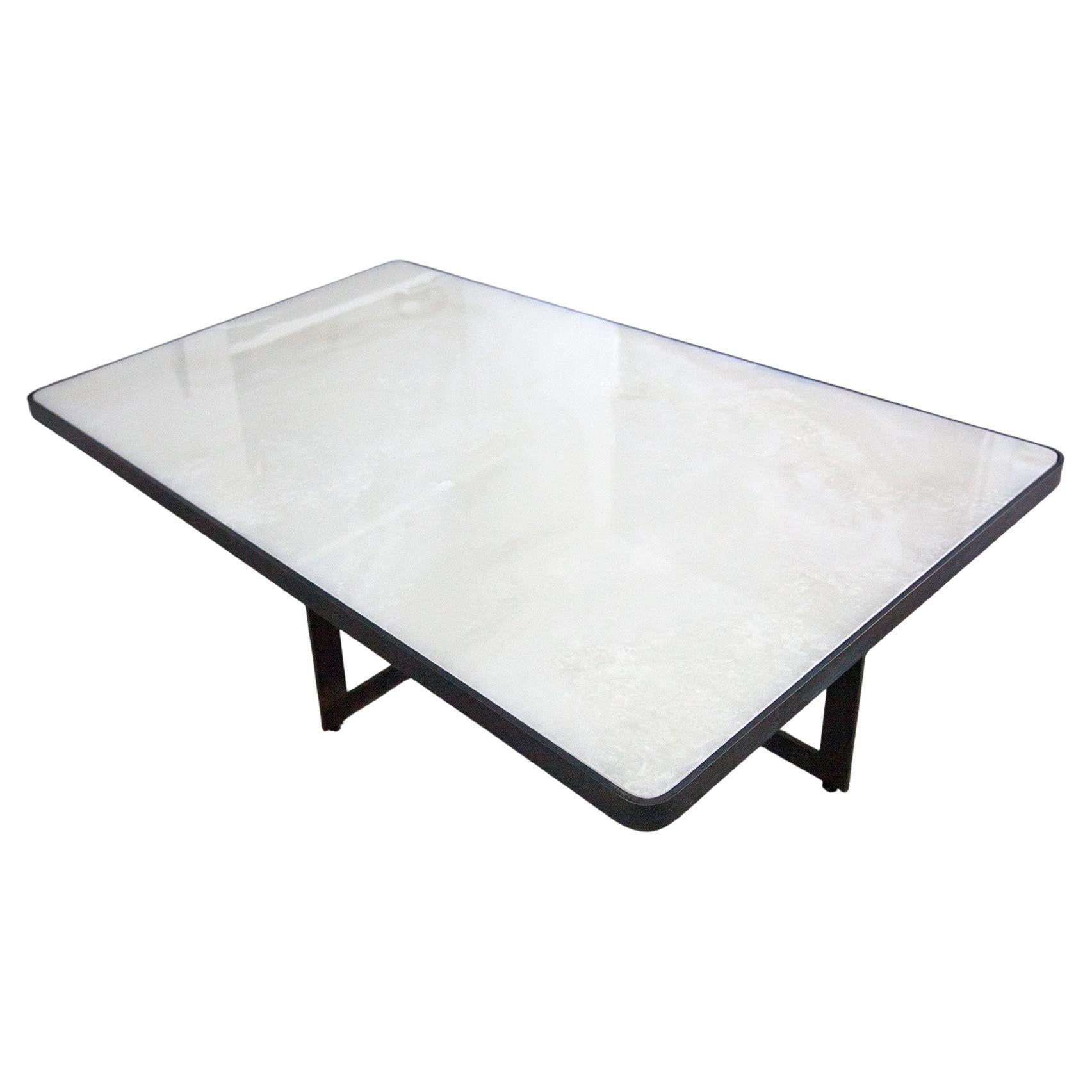 This stunning modern white quartzite coffee table with blackened steel base reflects a striking juxtaposition of materials and form. The luminous white quartzite is encased in molded blackened steel with a sleek steel cross base. While the steel
