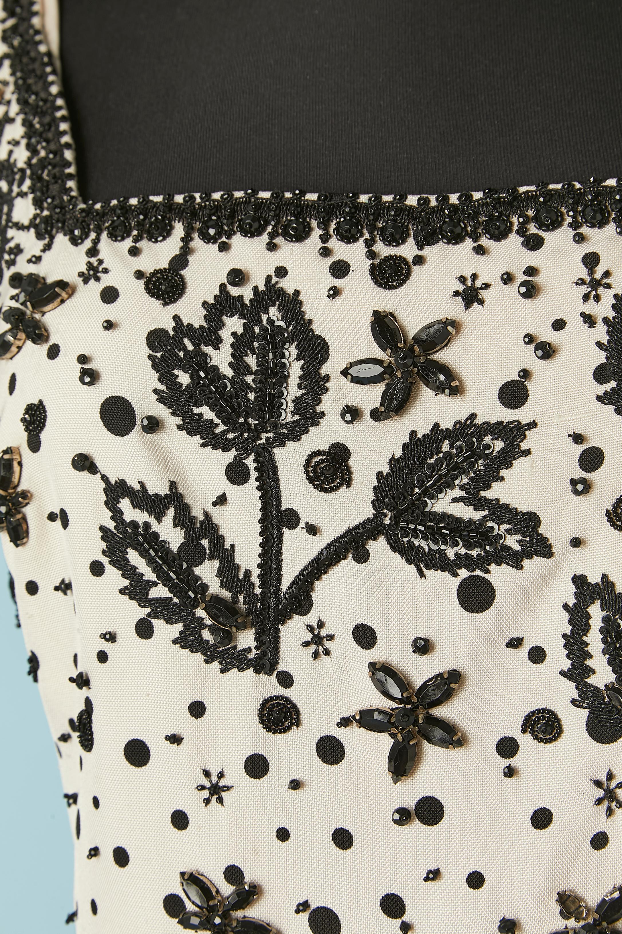 Vestido de cóctel de seda cruda blanca con lunares negros y bordados de hilo negro, cuentas y strass negro. 
No hay etiqueta de composición del tejido, pero el forro es de seda. Cierre con cremallera y corchetes en la parte central de la