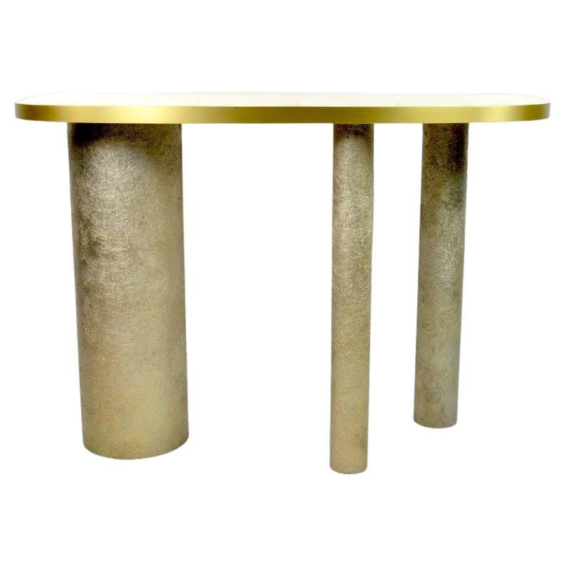 La table console Ovoid est composée d'un plateau en marqueterie de cristal de roche blanc.
Les bords du plateau sont en laiton brossé.
Il possède trois pieds cylindriques recouverts de fibre de verre semi-brut avec une patine dorée.

La partie