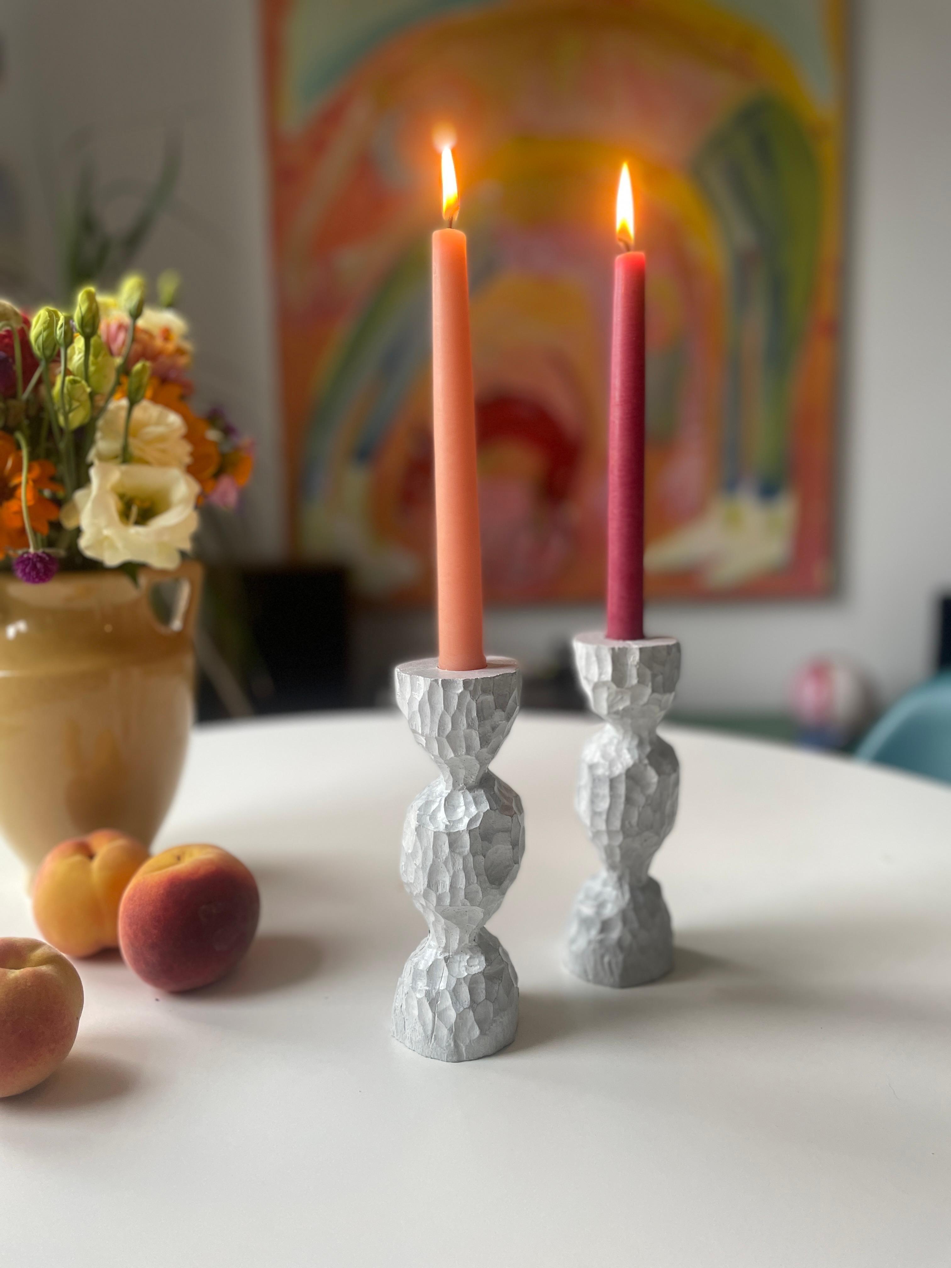 Originally carved in wood, these candlestick holders have been cast in concrete transferring the tool marks of the chiseled wood onto the surface of the concrete candlestick holder. 

Finished by hand with a pigmented wax creates unique variations
