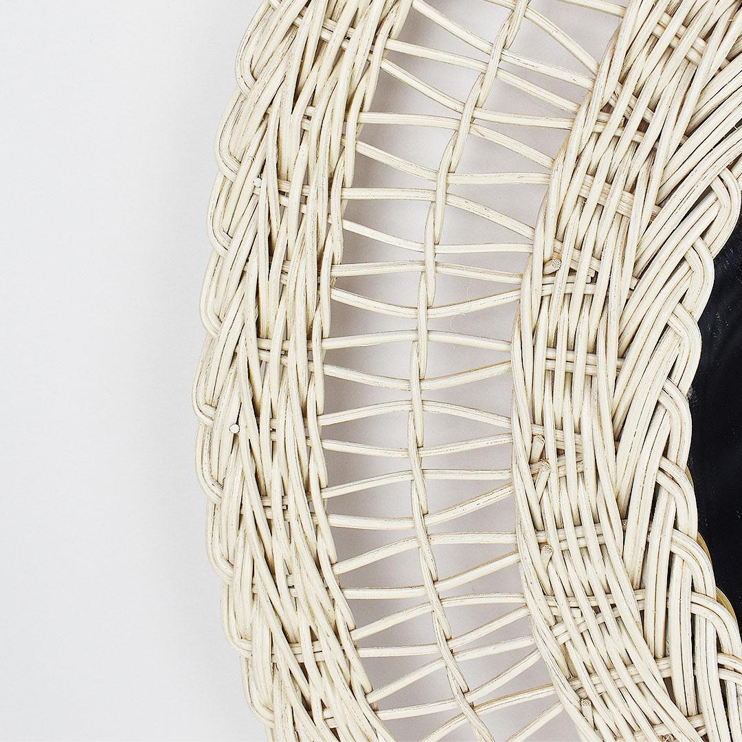 White round woven wicker and bamboo mirror with generous proportions. This mirror is created from a natural woven wicker in a round shape with varying types of weaving in concentric circles around the mirror at the center. 

At the back, a metal