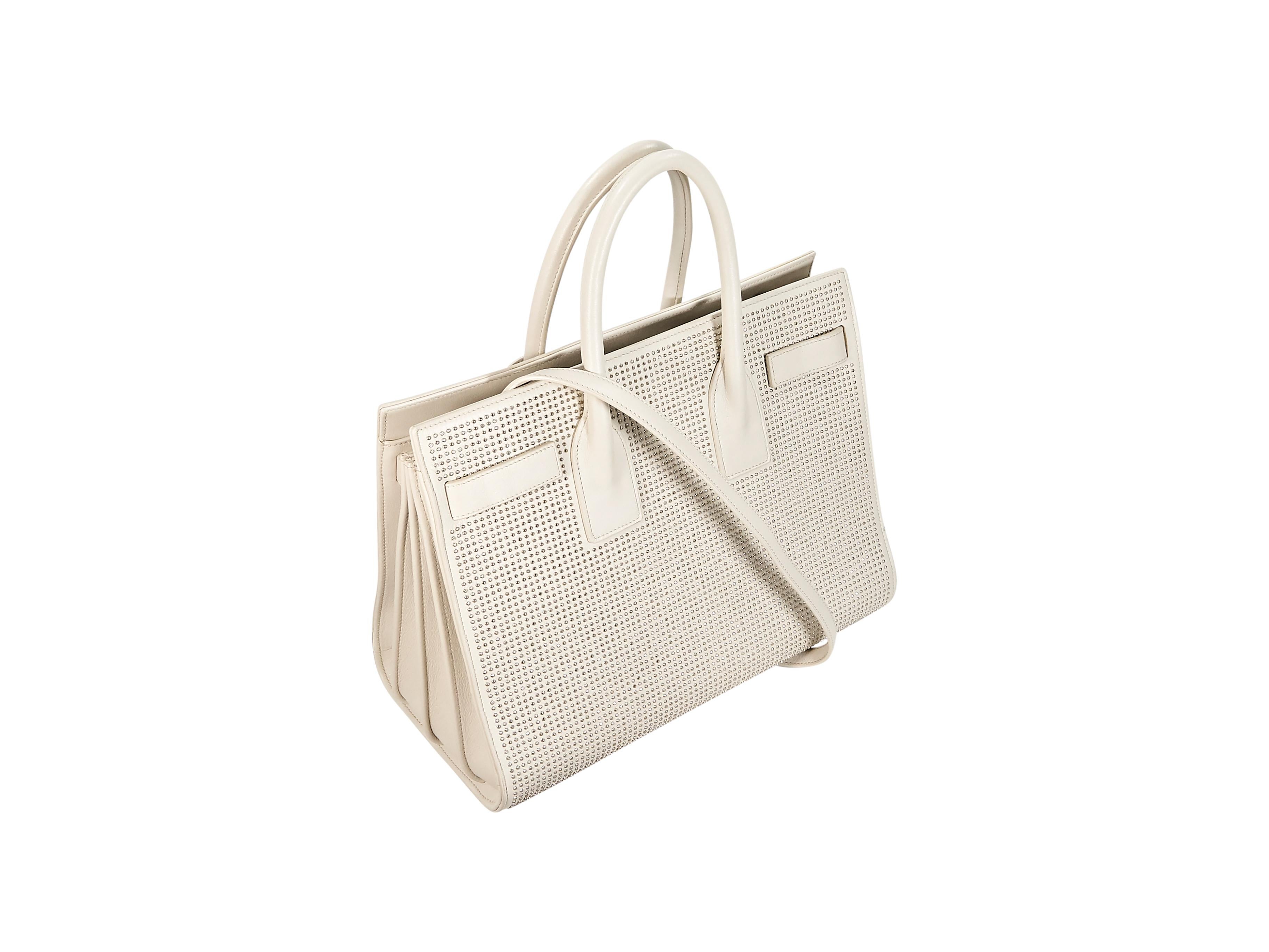 Product details:  White studded leather Sac de Jour satchel by Saint Laurent.  Dual top carry handles.  Detachable shoulder strap.  Open top.  Lined interior with center zip compartment and inner slide and zip pockets.  Protective metal feet. 