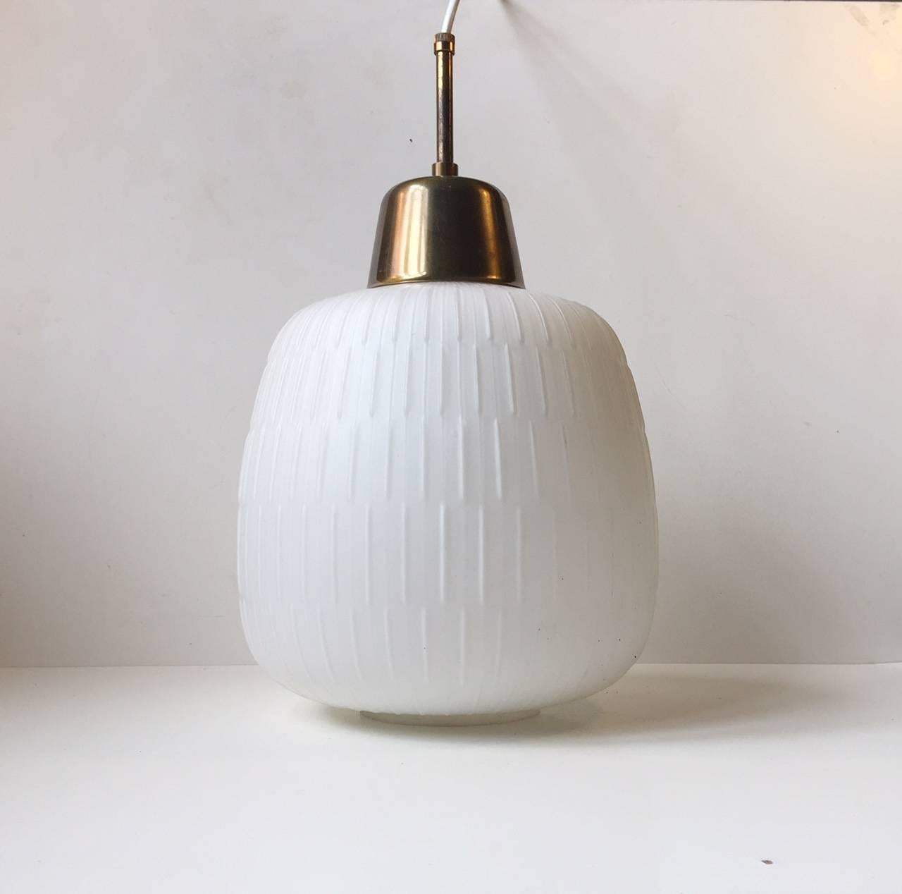 Grande lampada a sospensione a forma di zucca composta da vetro opalino opaco scanalato o molato con montatura e tubo in ottone. Prodotto e progettato in Scandinavia, probabilmente da Fog & Mørup o Luxus. Rimane in buone condizioni d'epoca con un