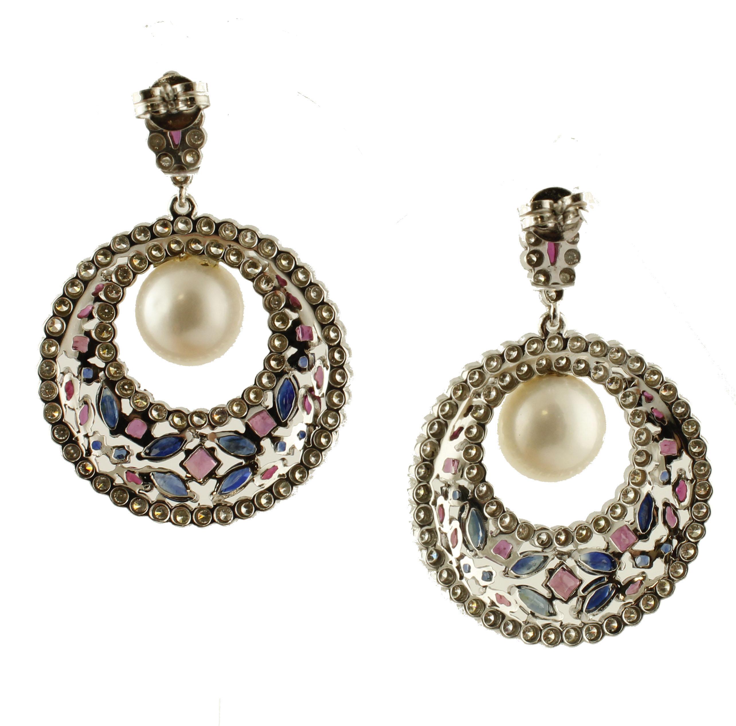 Precious dangle earrings mounted in 14k white gold structure. The tops -made of little rubies surrounded with diamonds- suspend two pierced circles studded with rubies,blue sapphires and beautiful white diamonds. The two holes hold two beautiful
