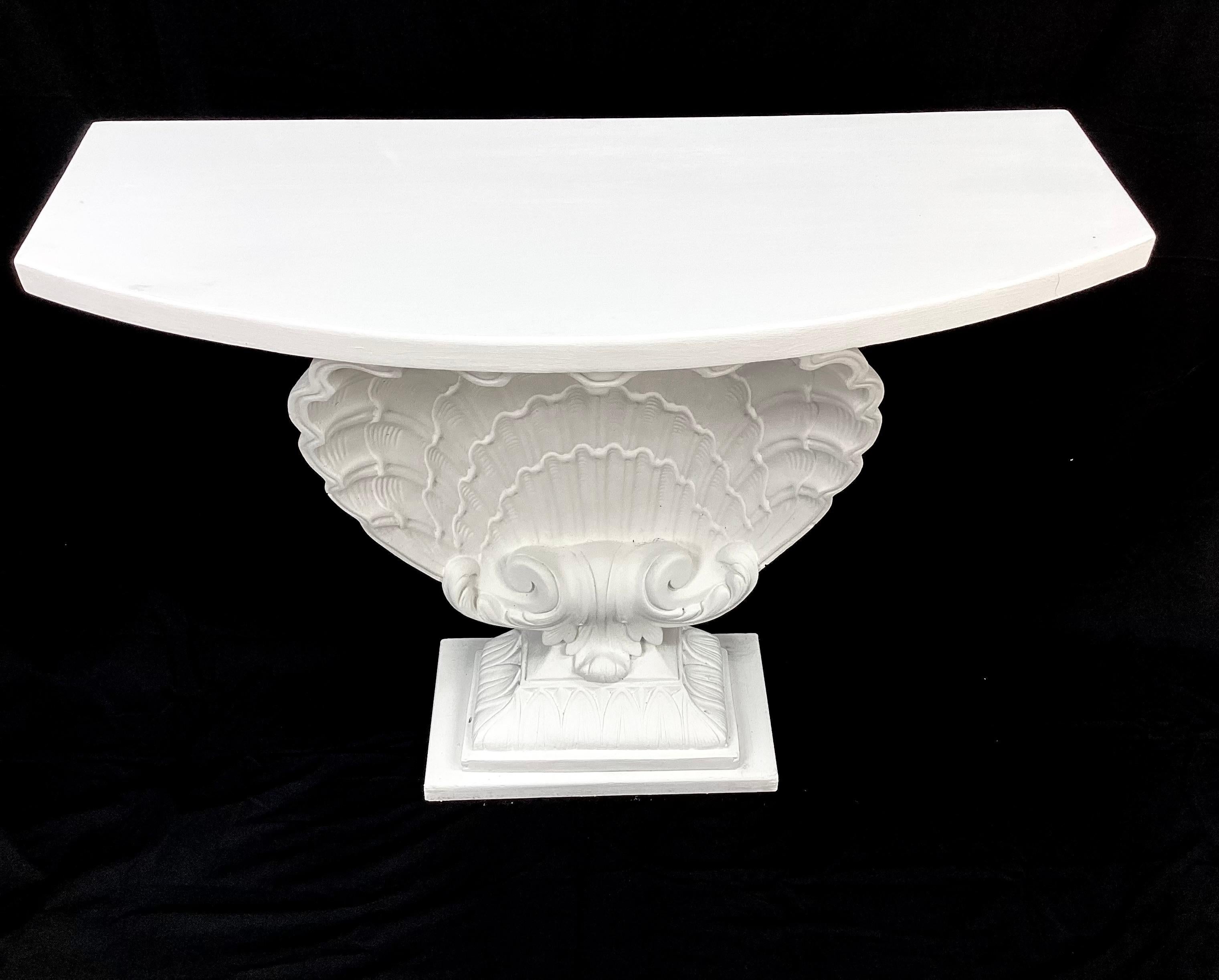 This is a beautiful classic Hollywood Regency style console table painted white in a flat finish, in the manner of Grosfeld House. The top front is rounded over a large plaster intricately detailed clam shell. Sturdy wood supports back of table. 