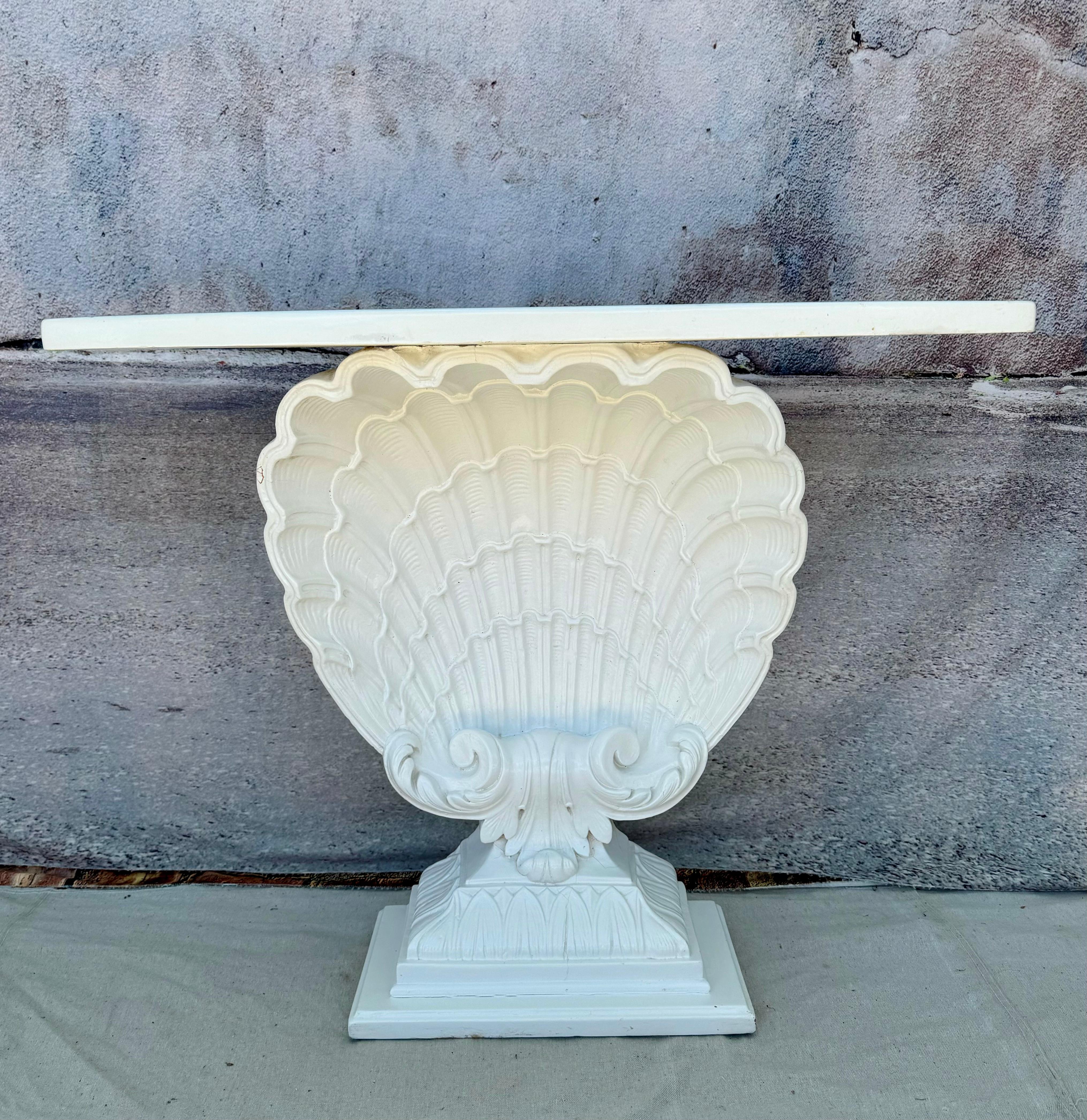 This is a beautiful classic Hollywood Regency style console table painted in a white finish, in the manner of Grosfeld House. The top front is rounded over a large intricately detailed clam shell. Sturdy wood supports back of table. 