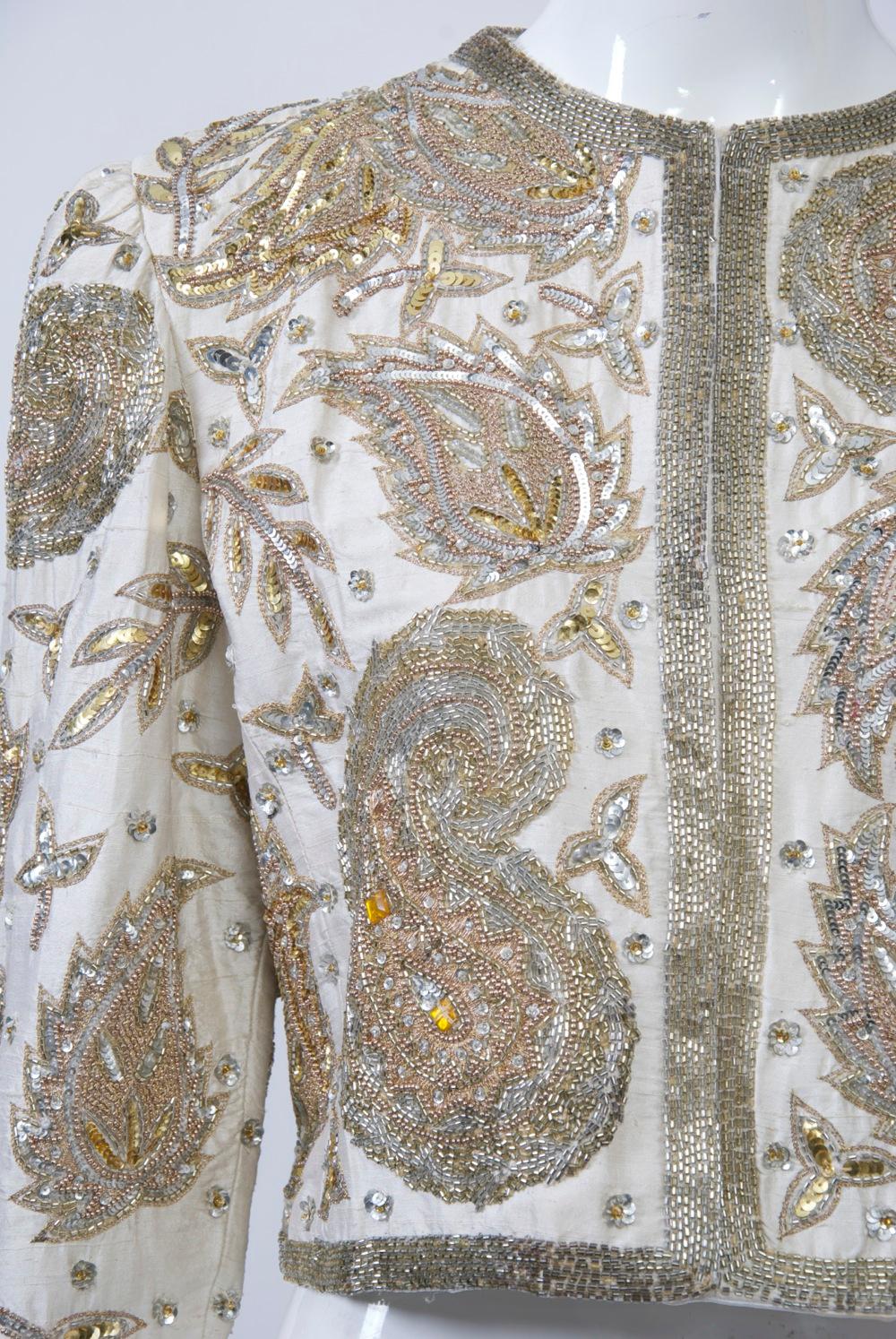 Bergdorf Goodman cropped evening jacket, the body of white silk heavily beaded in a paisley pattern with a variety of silver and gold beads and sequins punctuated with yellow and clear crystals at center. Set-in sleeves, collarless style ending at