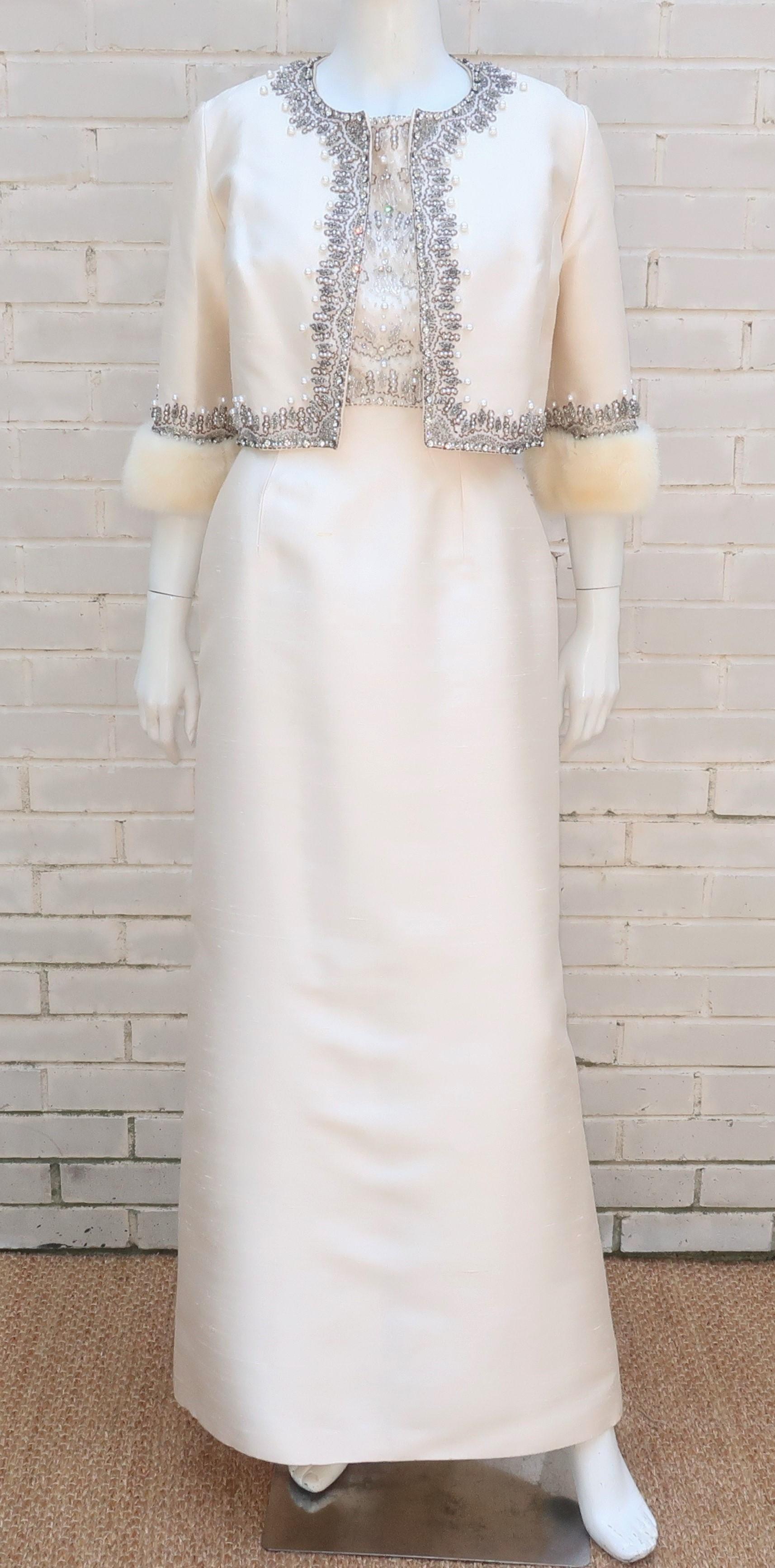 Regal 1960's white silk dupioni evening dress with ornately beaded bodice and coordinating cropped jacket trimmed at the cuffs in mink fur.  The sleeveless dress zips and hooks at the scooped neck back with a modified empire waist bodice embellished
