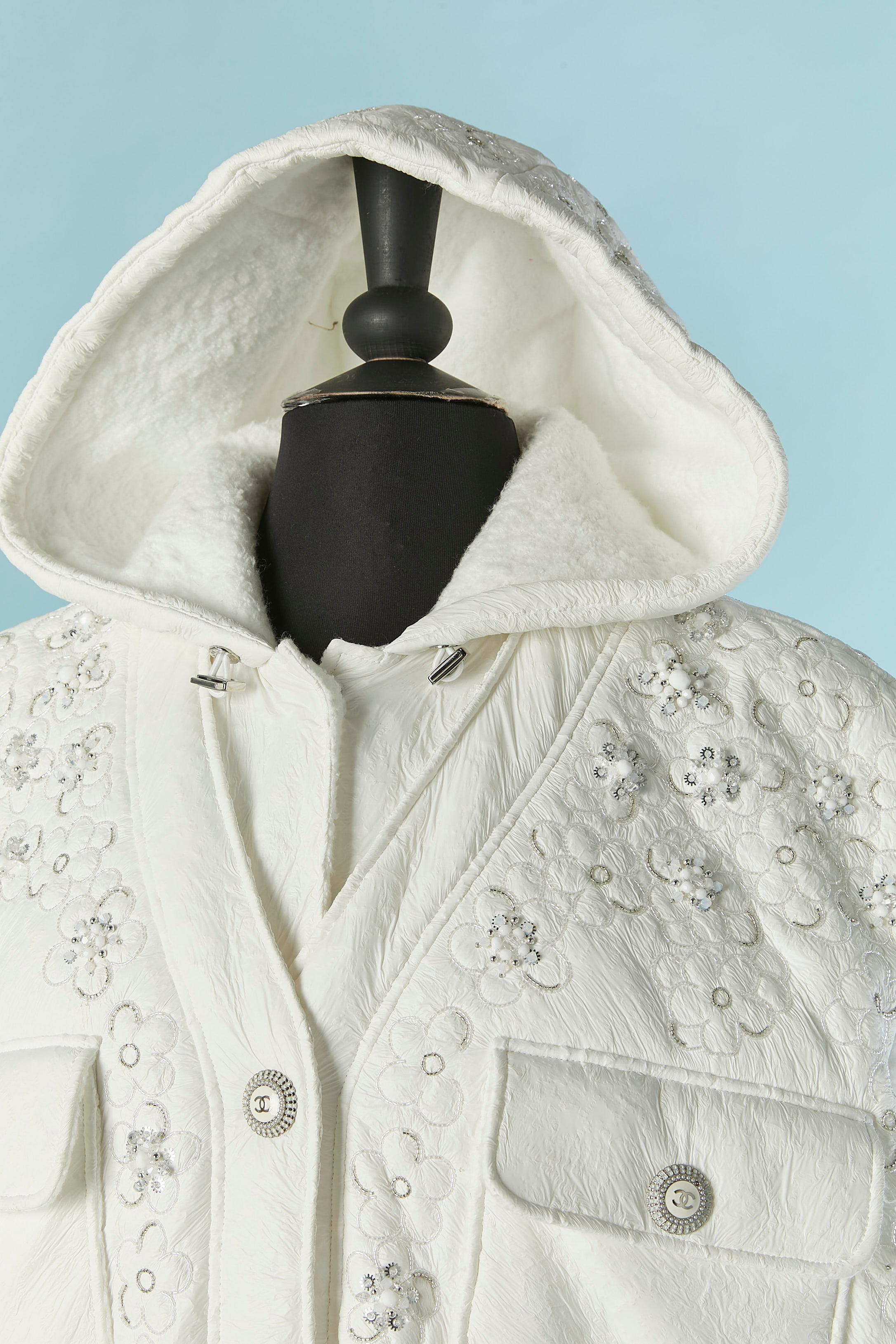 Veste blanche sans manches, légèrement paddée et enduite, avec capuche. Composition Coates : 100% polyuréthane Composition du support : 71% rayonne, 29% nylon. Padding : 100% polyester. 
Fermeture à bouton-pression sur le milieu du devant et sur le