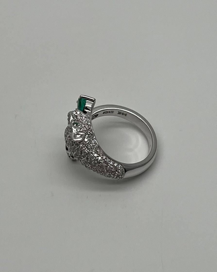 Un sorprendente anello Pantera Leopardo Whiting, con una testa di pantera meticolosamente lavorata, ornata da diamanti scintillanti e occhi di smeraldo verde vivo, incastonata in oro bianco lucido. La bocca della pantera stringe uno smeraldo