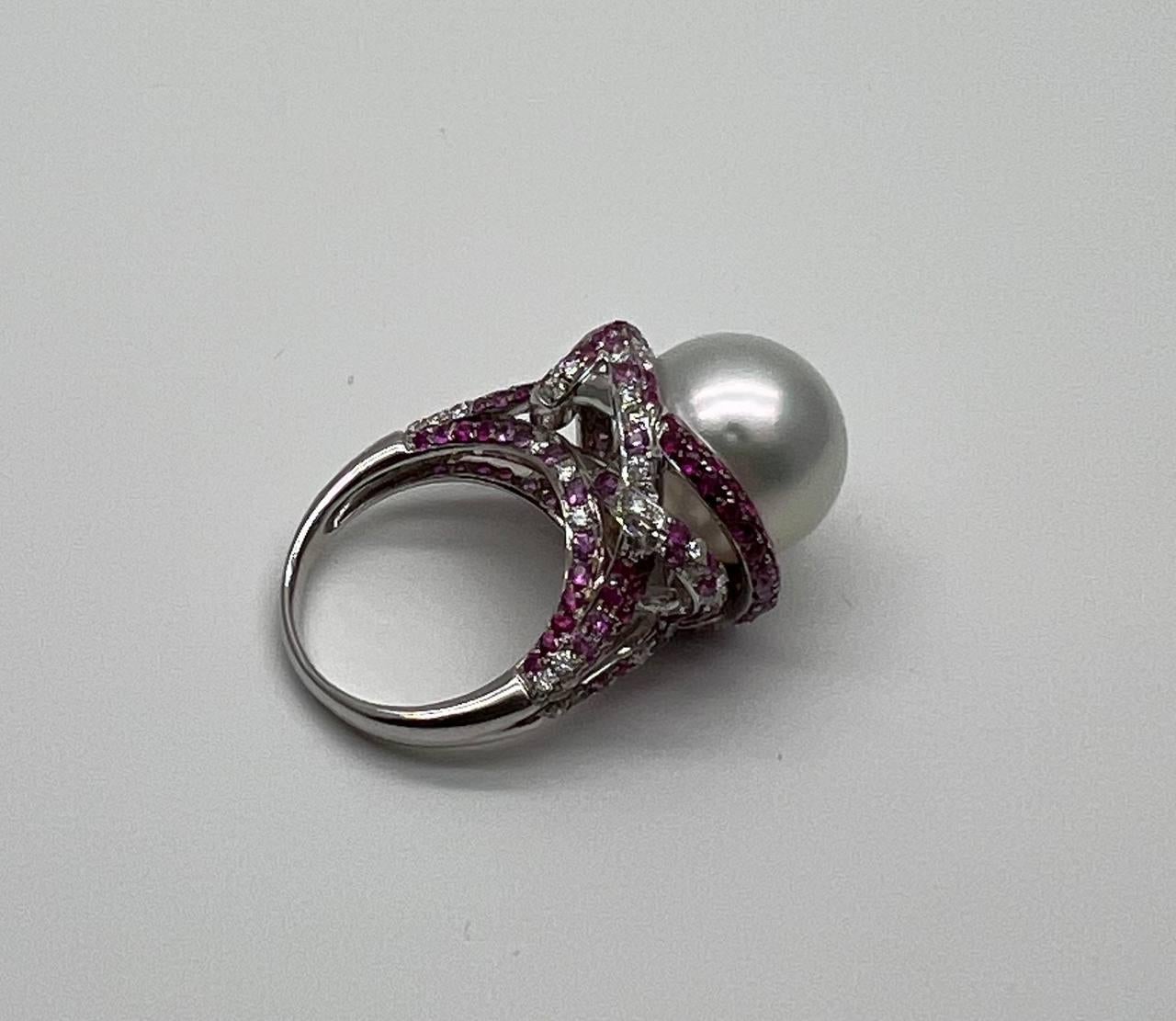 Questo anello di grande impatto presenta al centro una magnifica e luminosa perla bianca dei mari del sud. La perla è circondata da una serie di zaffiri rosa, rubini e diamanti bianchi che aggiungono un tocco di colore e raffinatezza. L'intricata