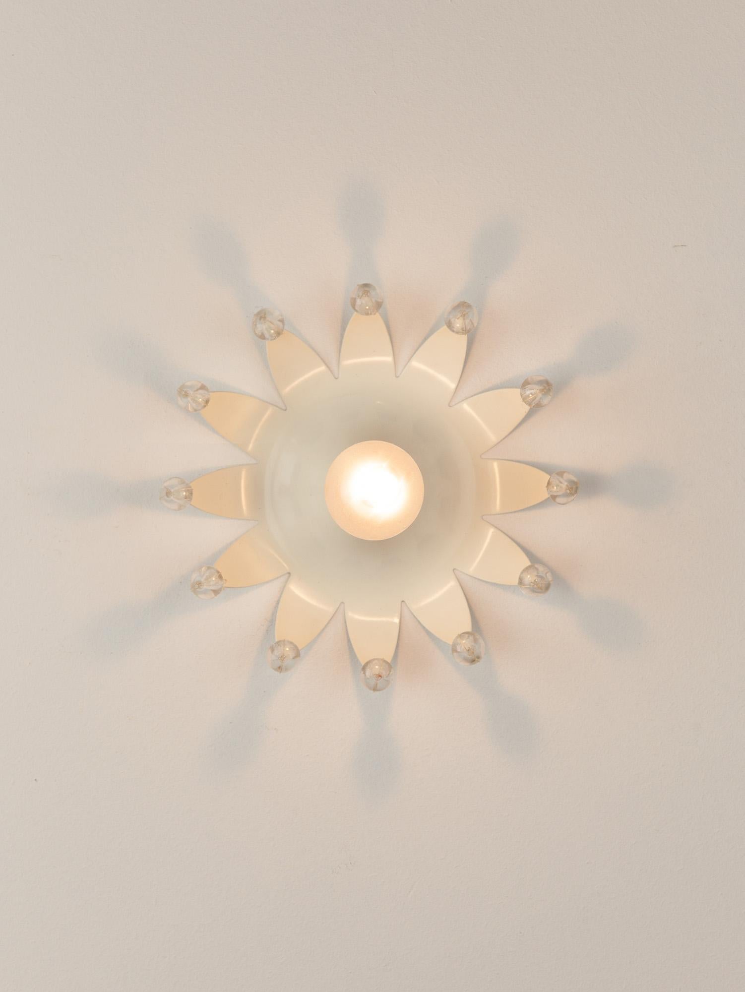 Rare and sweet Emil Stejner wall light for Rupert Nikoll with fine brass details. The petal shaped edge of the white-cream metal body is dotted with 12 clear acrylic spheres. Emitting a lovely starburst pattern from it's playful shape the wall light