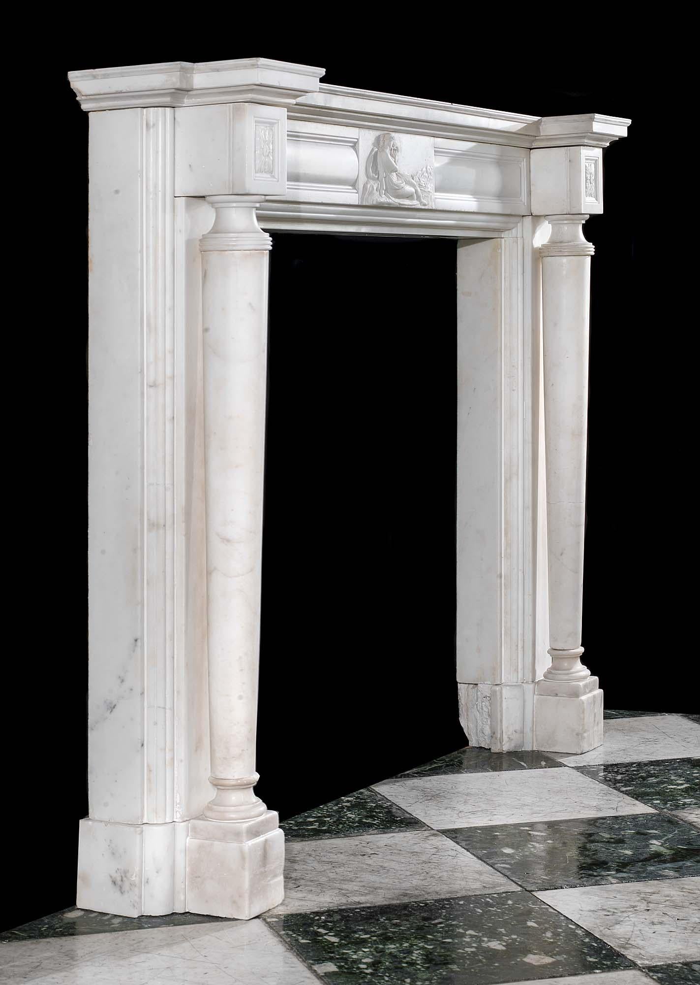 A small and elegant white statuary marble columned Regency antique chimneypiece. The wide corniced shelf resting above a cushion panelled frieze centred by a carved tablet depicting a Greek muse playing a lyre, is flanked by panelled foliate paterea