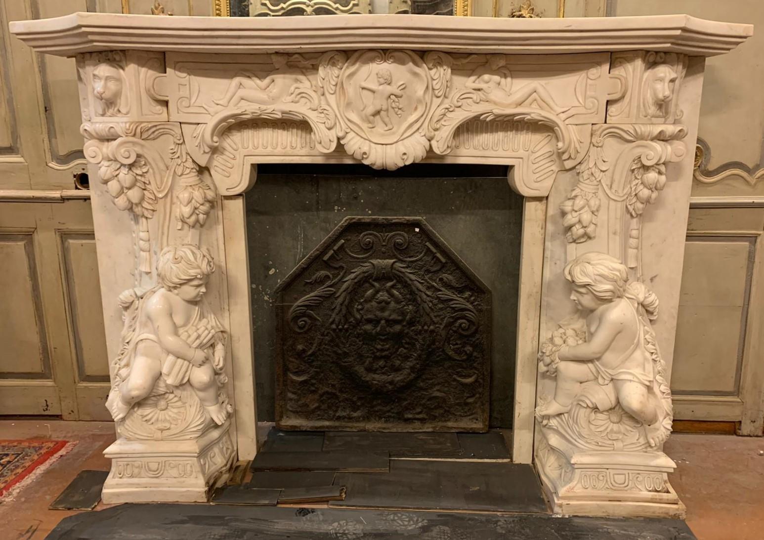 Old fireplace in statuary white marble, richly carved with cherubs, cupid in a central shell and dogs, coming from an important villa in Italy, built in the 1900s therefore not ancient even if very very rich and full of decorations, which denote the