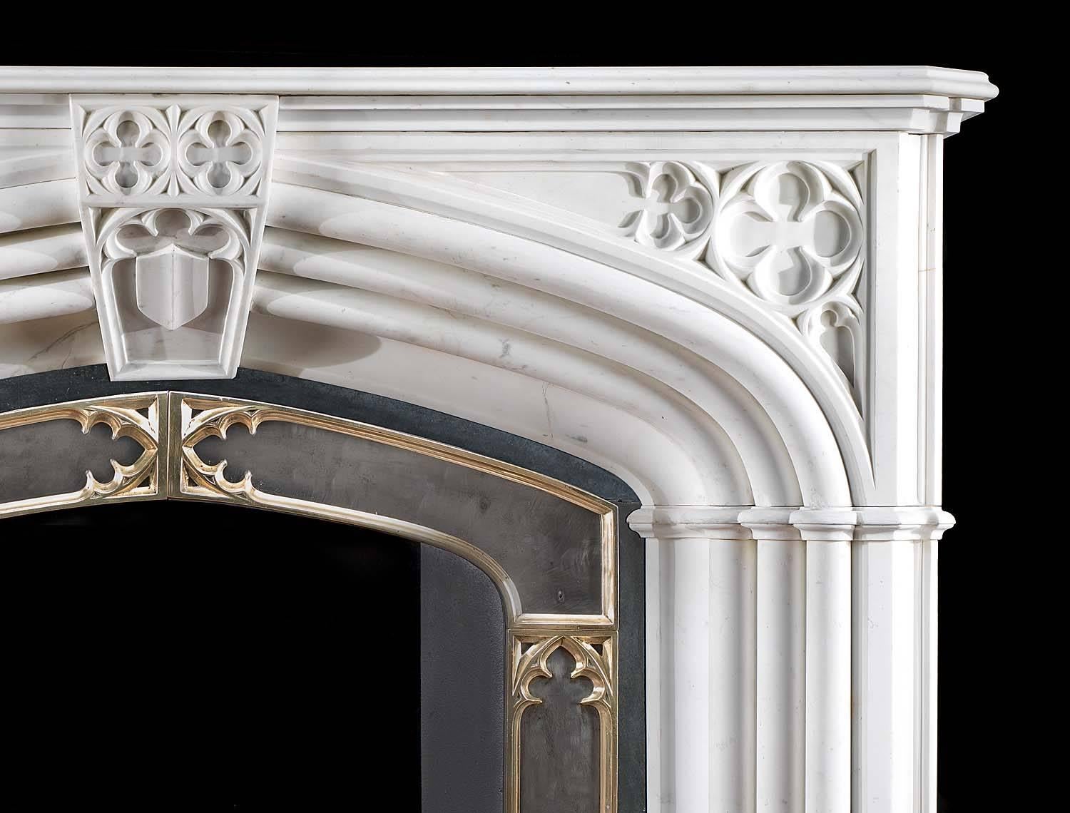 A large and imposing white statuary marble Gothic Revival chimneypiece together with it's original cast iron and brass-mounted insert. The shaped moulded shelf rests above triple columns which frame the slow arched opening and are linked by a large