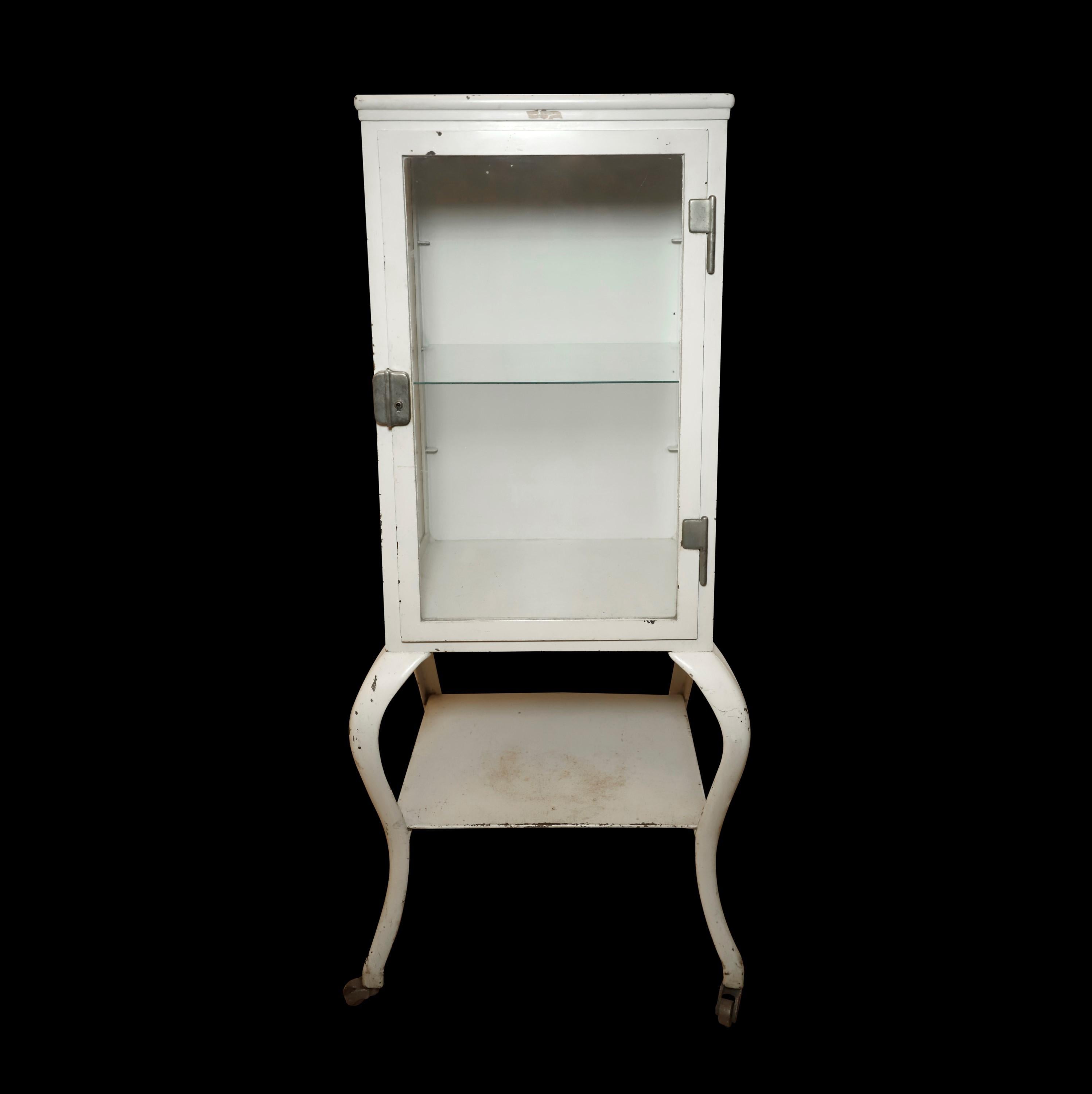 Early 20th century dental or medical cabinet. The cabinet itself is steel with glass sides, front door and one adjustable glass shelf. The cabriole legs are cast iron. Bottom shelf is sheet steel. Still with original white finish and original
