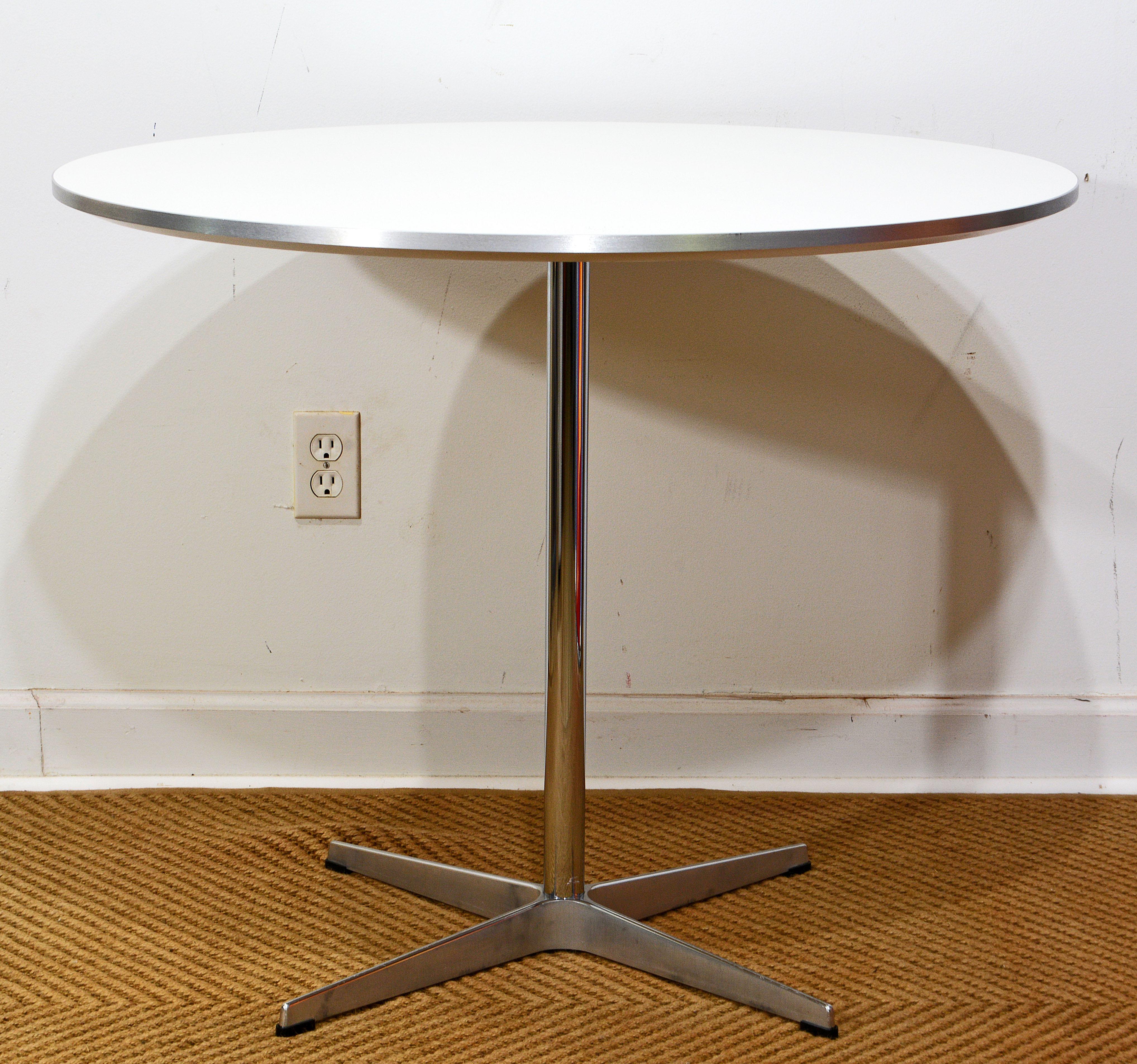 Ikonischer runder Café- oder Frühstückstisch, entworfen von Arne Jacobsen und hergestellt von Fritz Hansen im Jahr 2010. Der Tisch hat eine weiße, abgeschrägte Laminatplatte mit gebürsteter Aluminiumkante und eine polierte Aluminiumkonsole mit vier