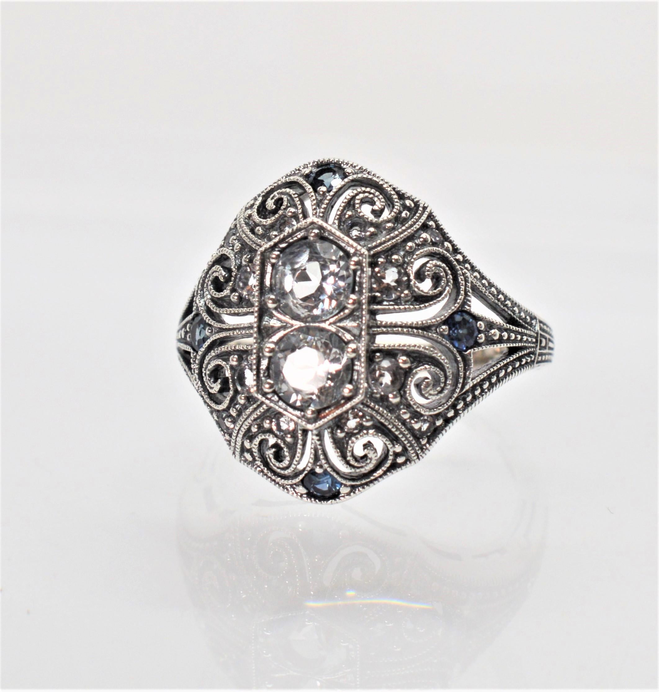 Enjoy this timeless vintage design with exquisite sterling silver filigree detail reminiscent of the Art Deco Period. This dome style ring has twin .20 carat round faceted white topaz center stones, .40 carats TW,  and is accented with tiny blue