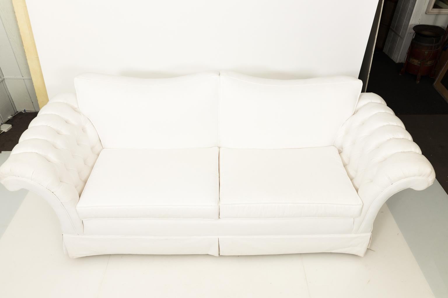Contemporary white custom built sofa with two cushions and rolled back armrests with tuffted sides.
 