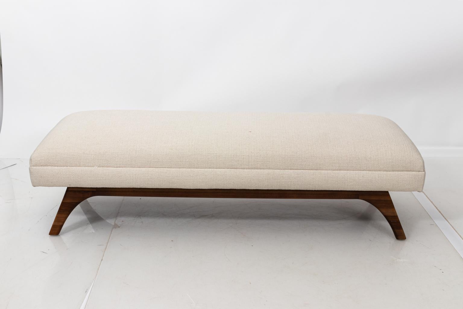 Mid-Century Modern style white upholstered bench with wood legs, circa 21st century. Please note of wear consistent with age including minor staining on the white upholstery and minor wear on the wood legs.