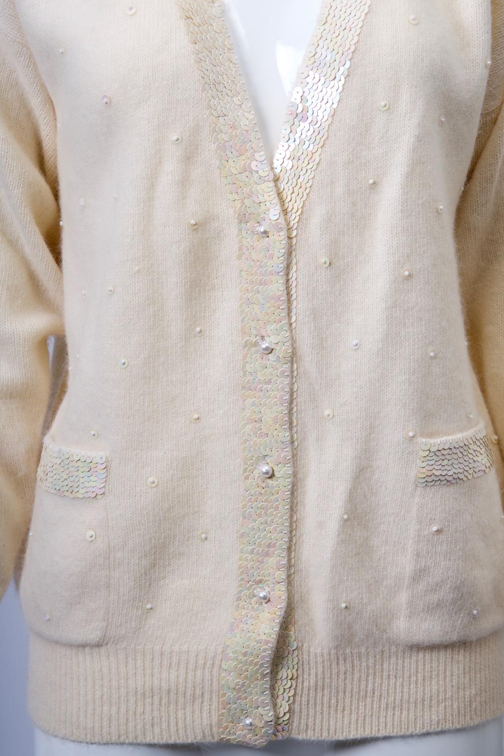 Cardigan à col en V en laine/angora mélangée, avec une bande de paillettes blanches irisées sur les bords du devant et sur les poches plaquées. Le devant du pull est également orné de perles éparses et fermé par des boutons en perles. Manches raglan