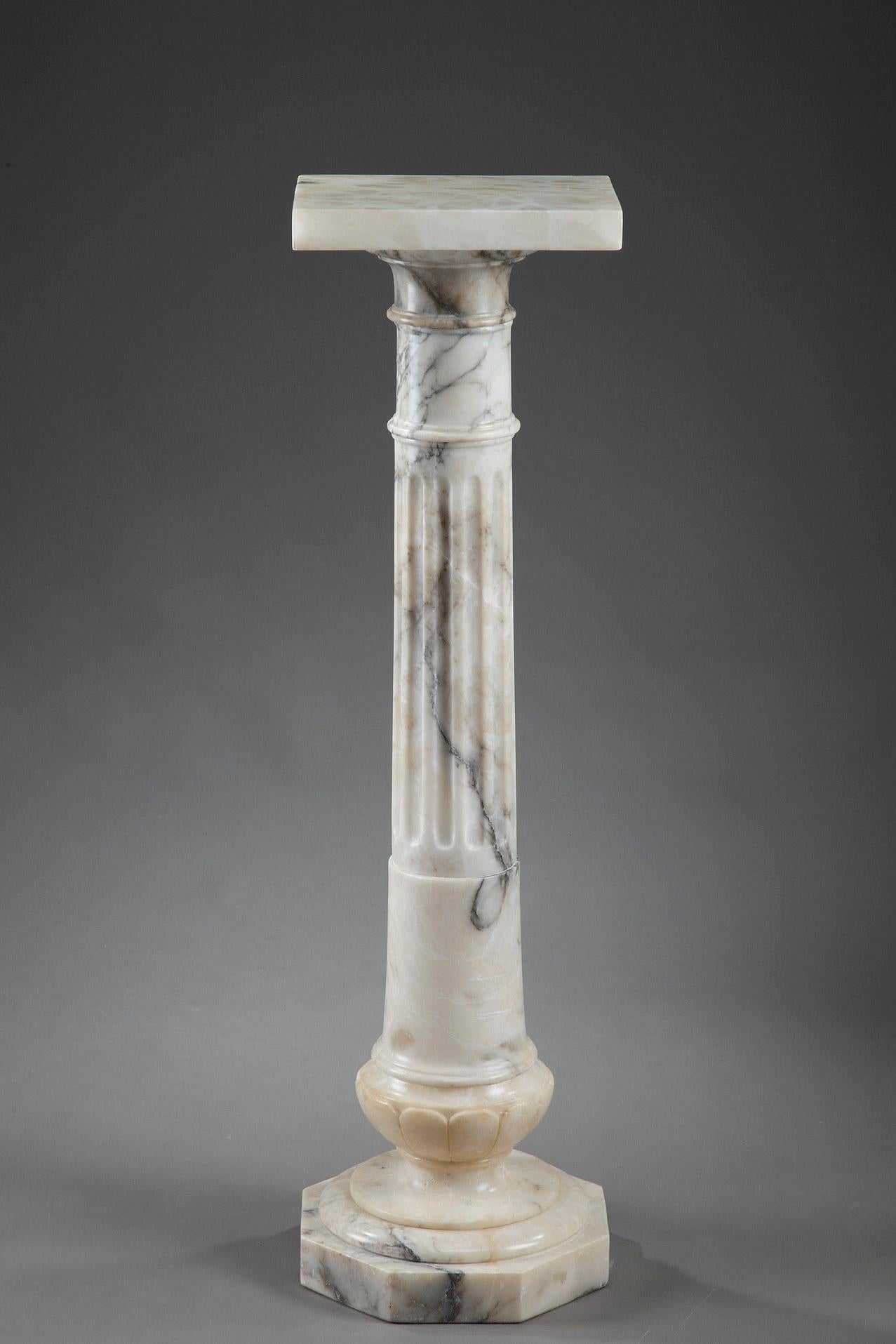 This is a white veined marble pedestal in the form of a column with a fluted shaft. The ringed capital is covered with a square top where a sculpture or clock can be placed. The feet of this pedestal are decorated with prominent gadroons and it