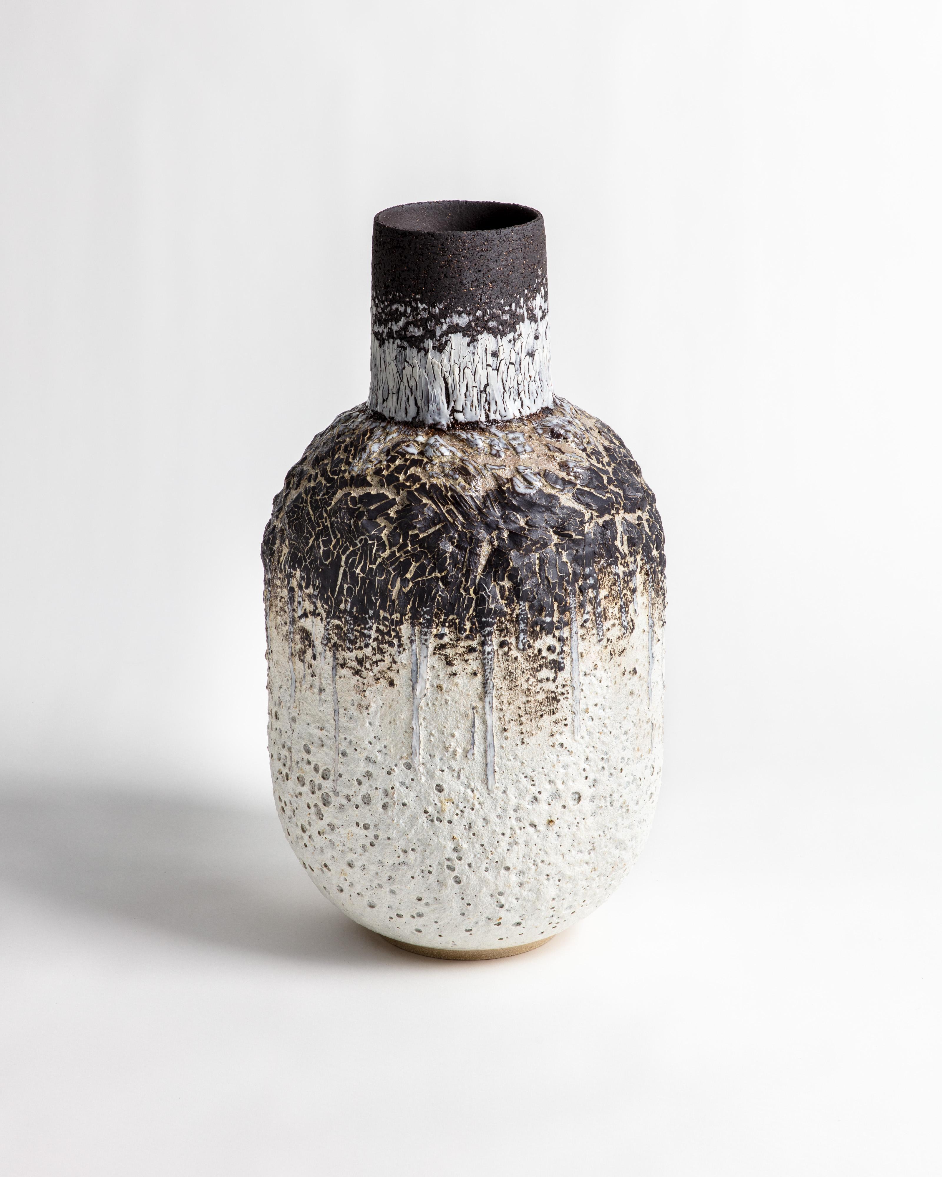 Tall large bottle shaped white and black stoneware clay and porcelain vessel with heavy volcanic textured glaze and black porcelain crackle.

The work is hand built using a combination of stoneware black and buff clays, volcanic slips are added