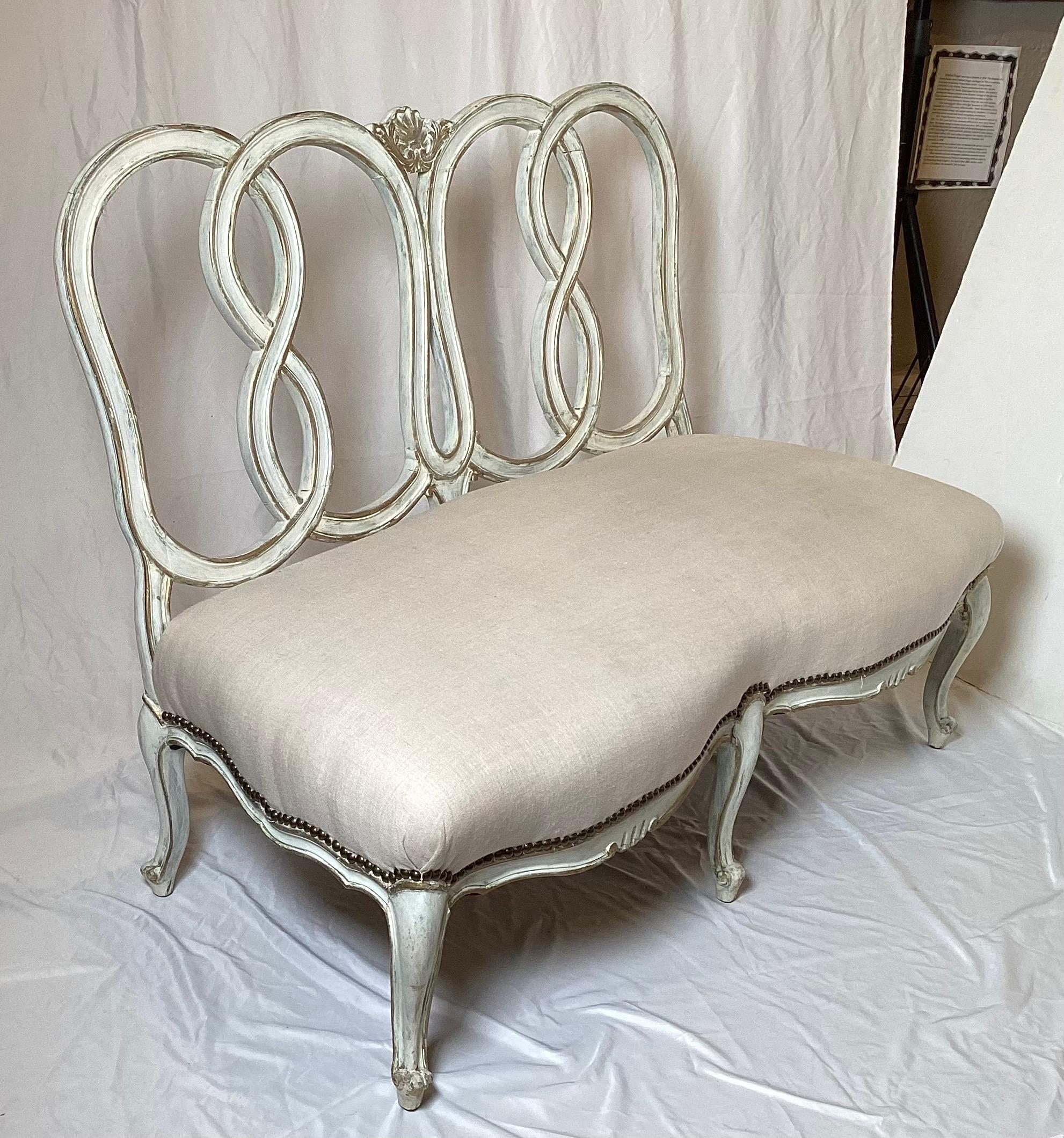 Un élégant canapé sans accoudoirs de style provincial français, tapissé d'une armature en bois blanchi.  La taille réduite, 44 pouces de long, avec un siège en lin nouvellement recouvert avec une garniture de tête de clou en laiton.  Il y a un léger