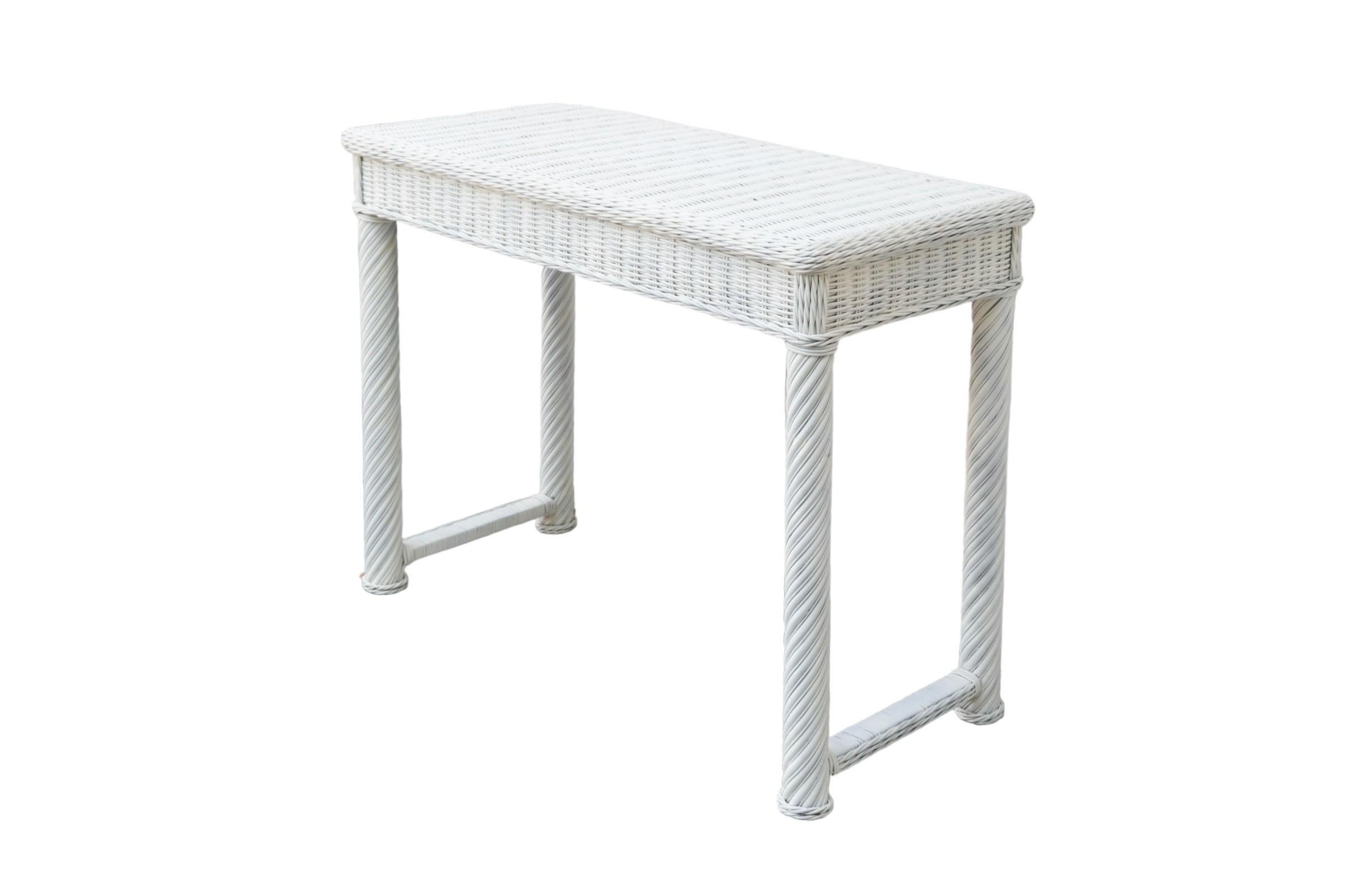 A white wicker woven hall table made of rattan. The table top is framed with a braided edge, and wooden legs and stretchers at each end are wrapped with rattan. Painted white throughout.